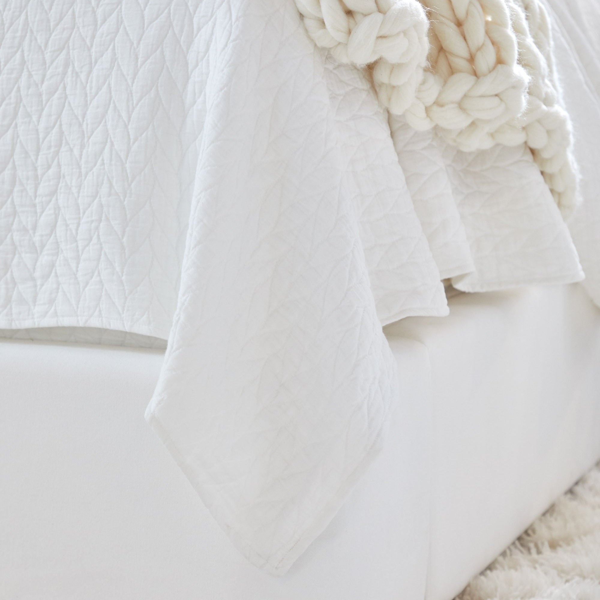 Close-up of white quilted bedspread on Balboa Queen Bed by Essentials for Living showcasing soft neutral tones and texture.