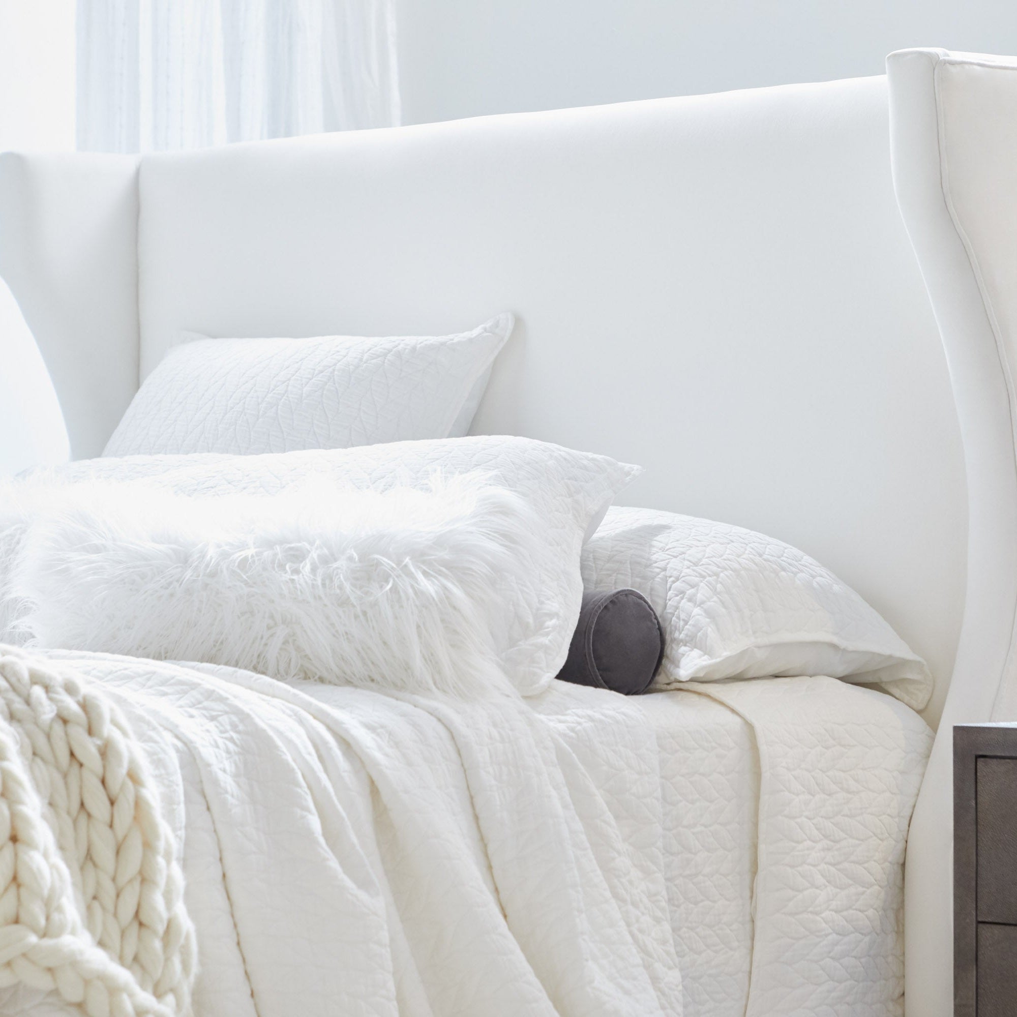 Close-up of white upholstered Balboa Cal King Bed with wingback headboard and textured bedding by Essentials for Living
