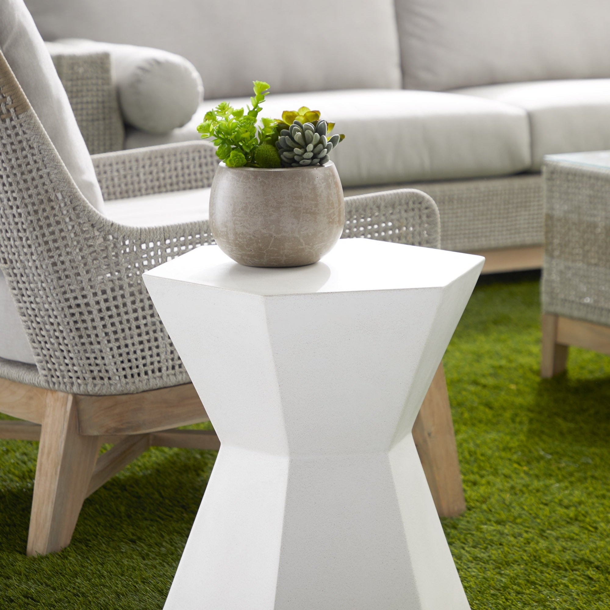 Bento Accent Table in white with sculptural hourglass shape beside woven chair in outdoor setting Essentials for Living