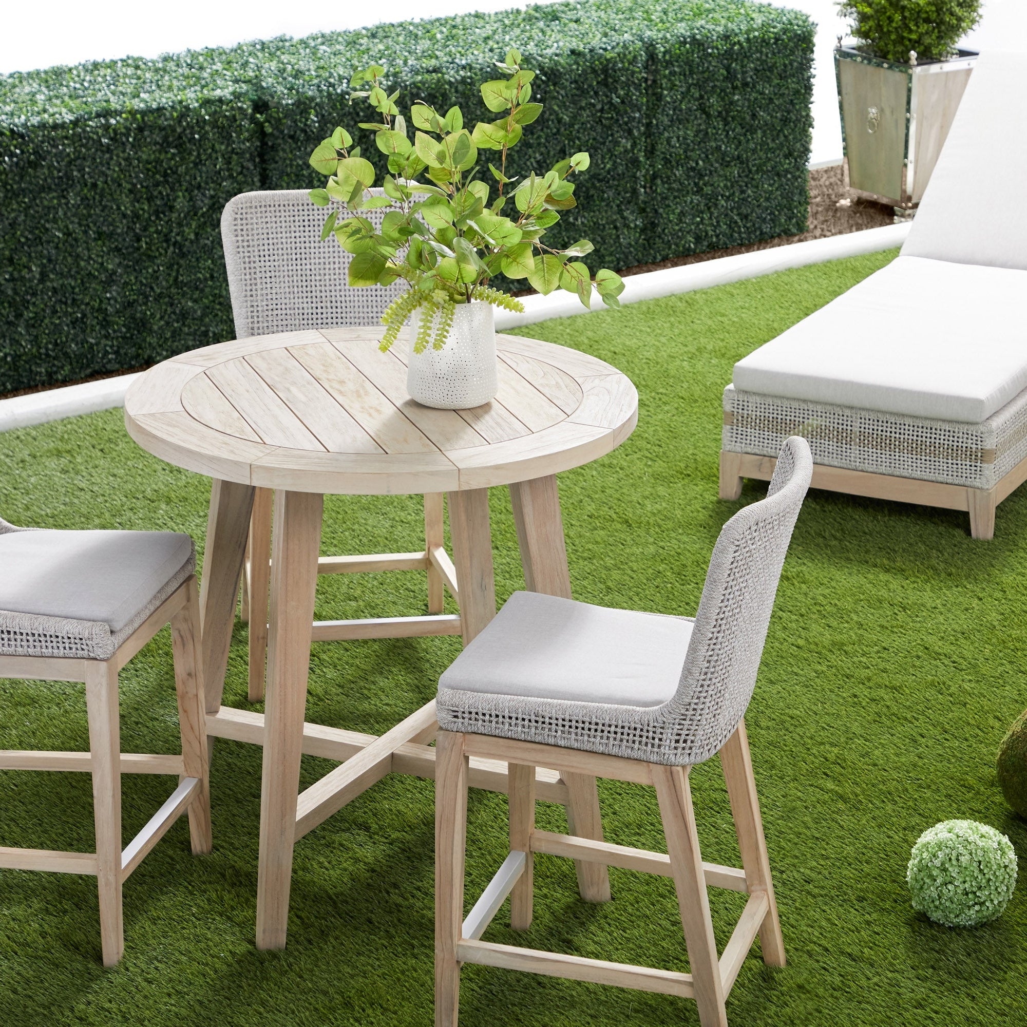 Round wooden patio table with plant centerpiece and wicker chairs on green grass outdoor setting Essentials for Living Bento Accent Table