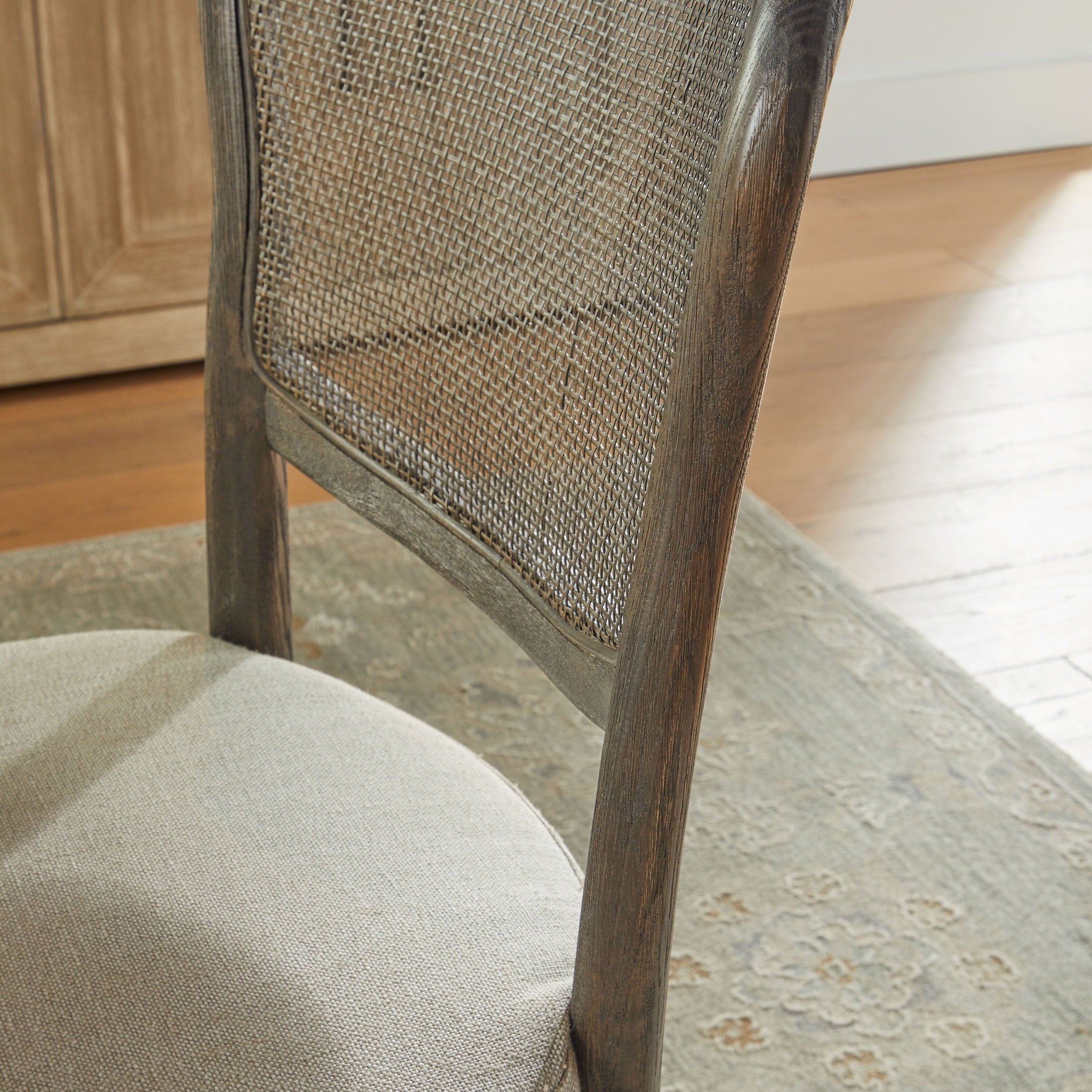Close-up of Essentials for Living Cela Dining Chair with handwoven cane back and bisque upholstered seat