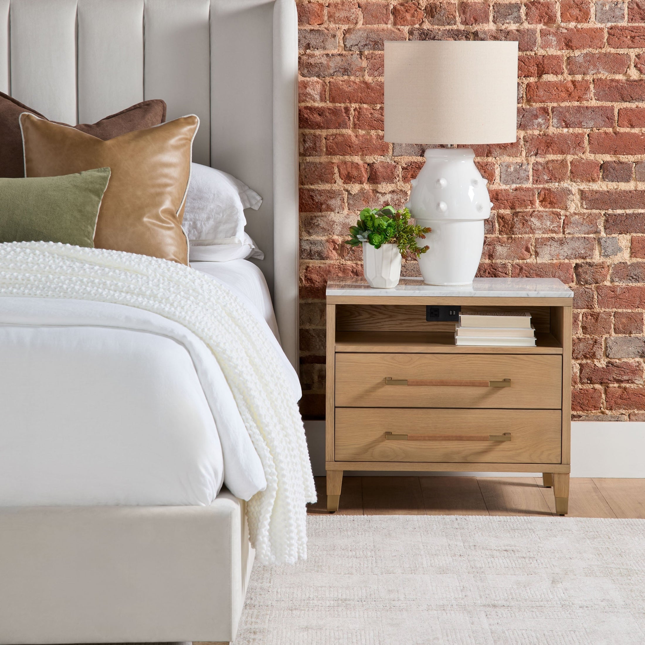 Chandler Standard King Bed in cream velvet with wingback headboard next to oak nightstand and brick wall background