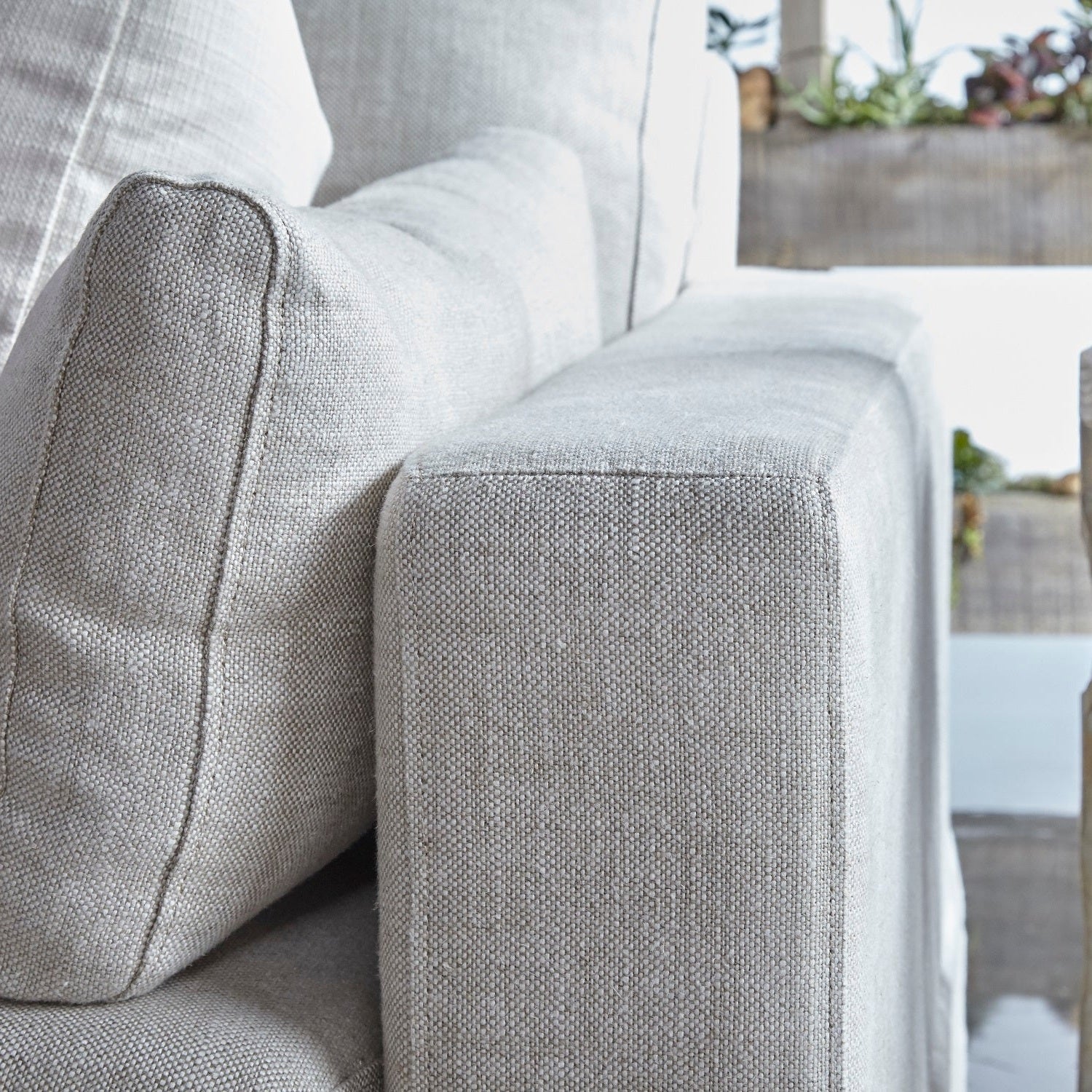 Close-up of light gray fabric sofa armrest and cushions with soft texture in a bright living room setting