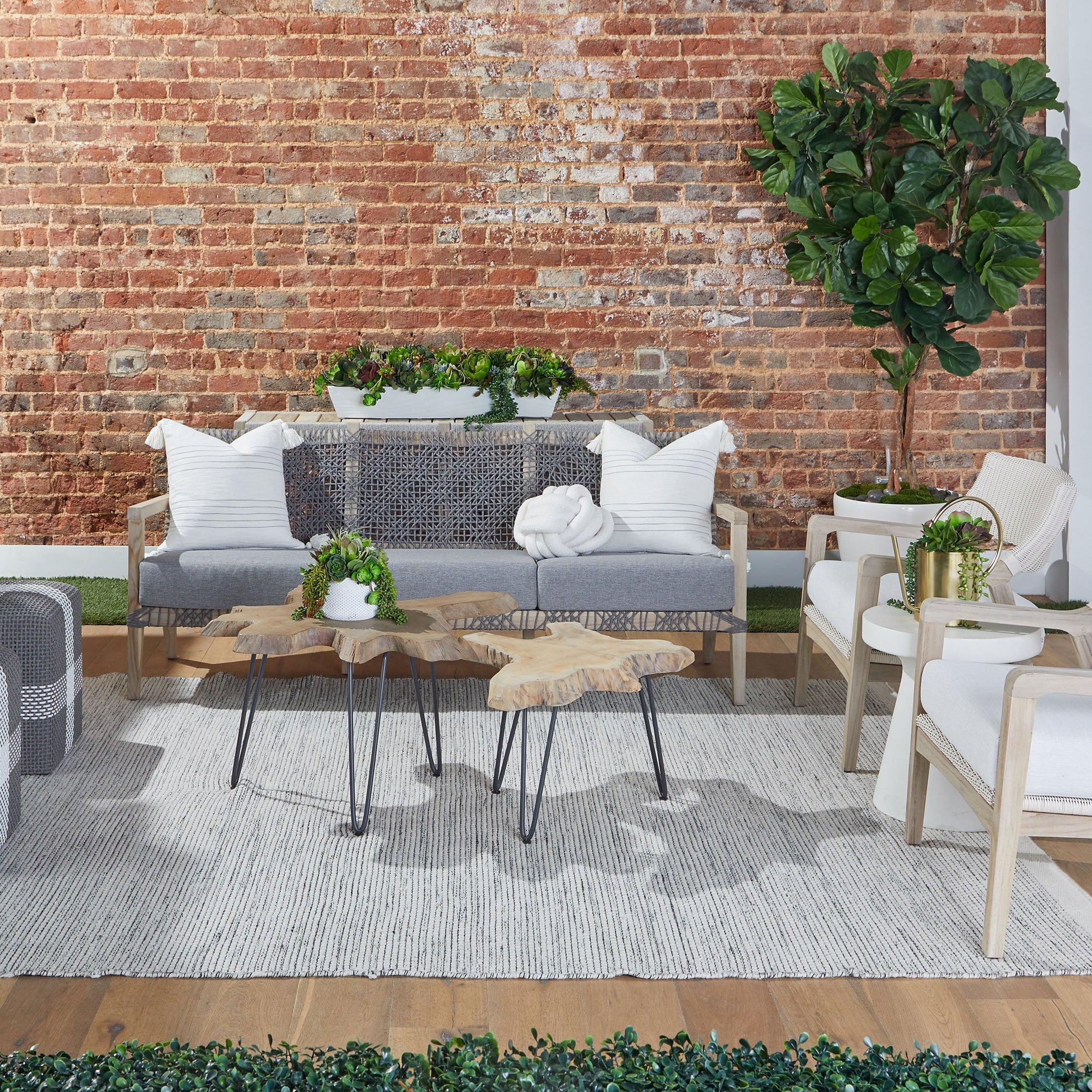 Modern outdoor seating area with taupe and white rope woven sofas and wooden accent tables on a gray rug