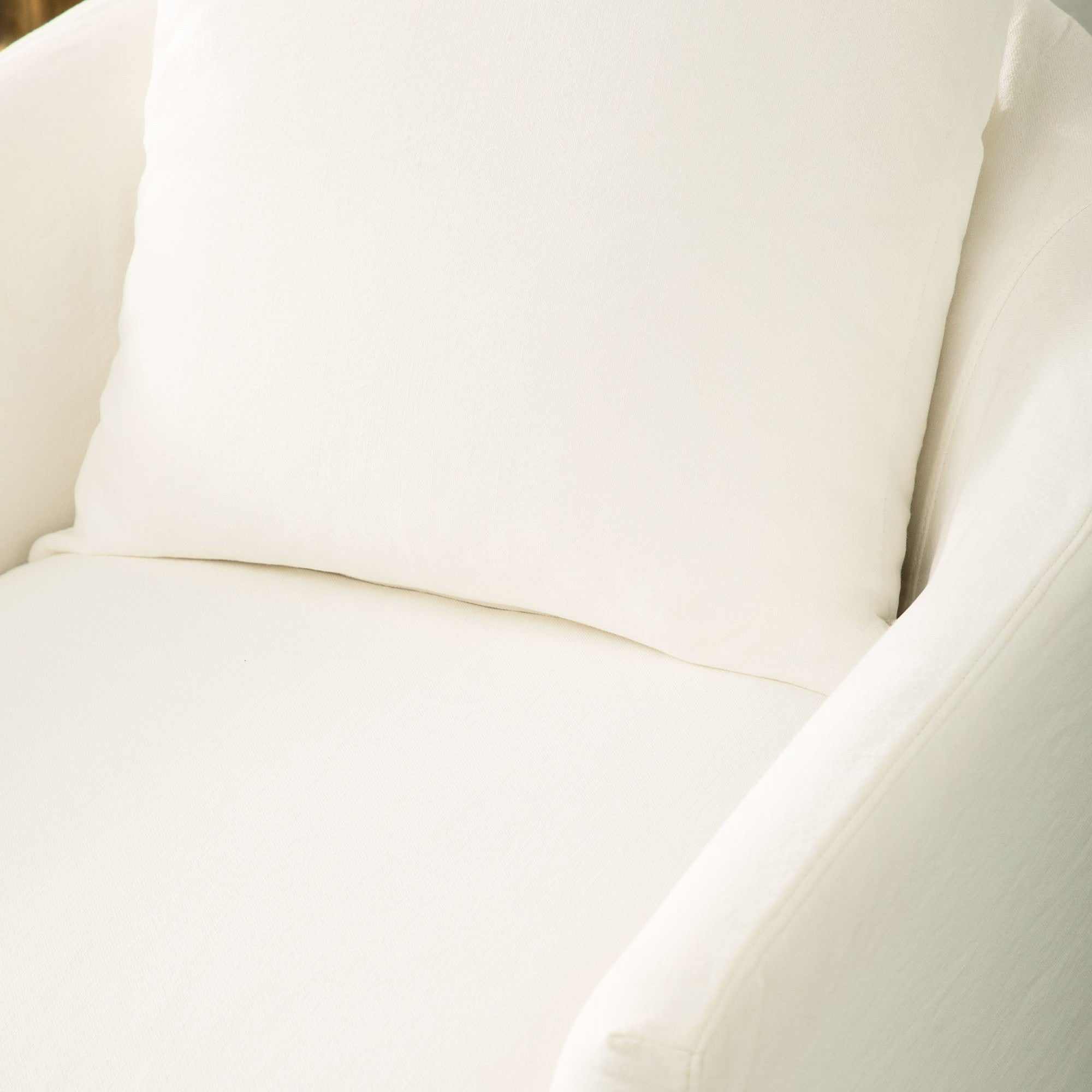 Close-up of a creamy white slipcovered swivel club chair with matching plush throw pillow by Essentials for Living