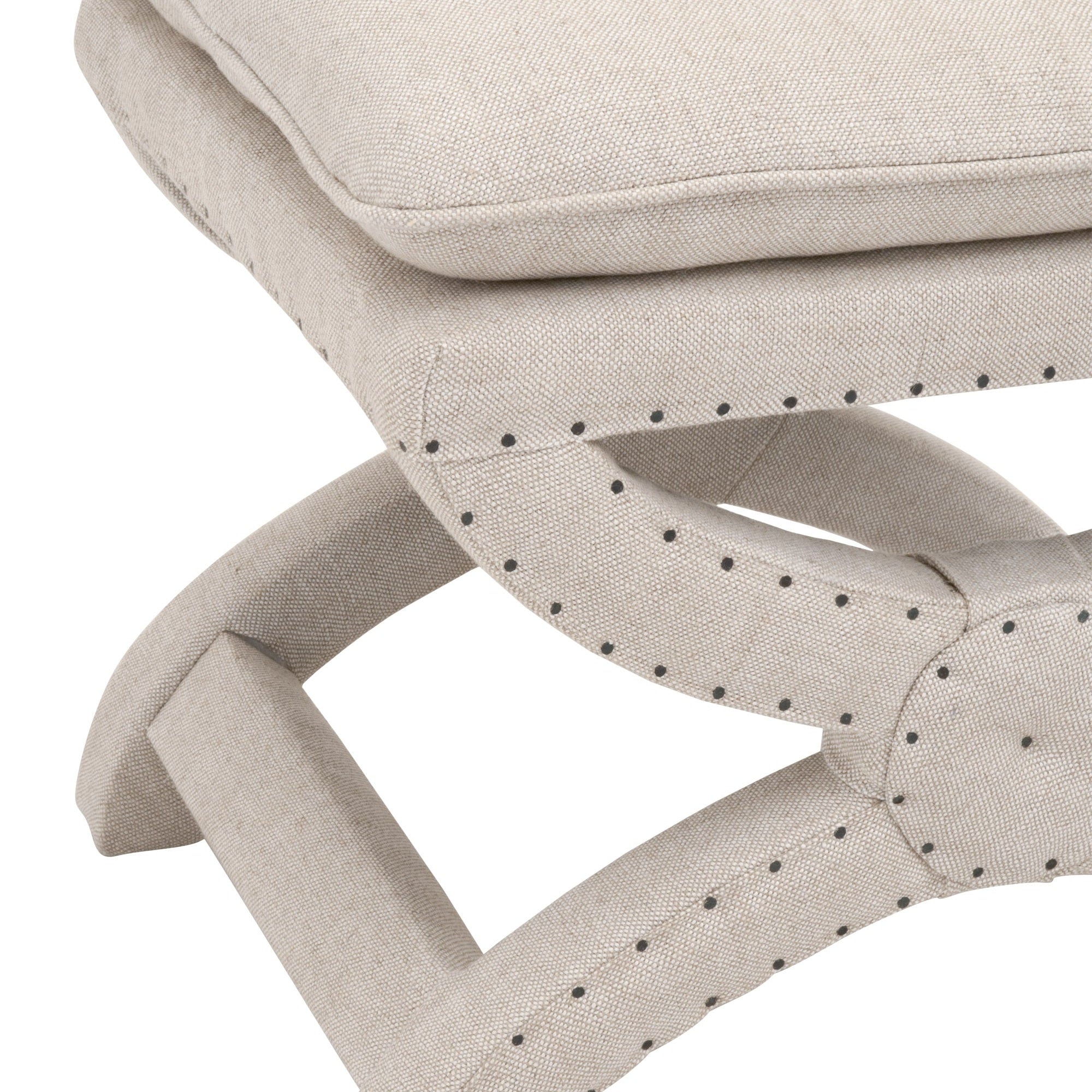Close-up of Gaston Ottoman in creamy beige performance linen with black nailhead trim and unique X base design