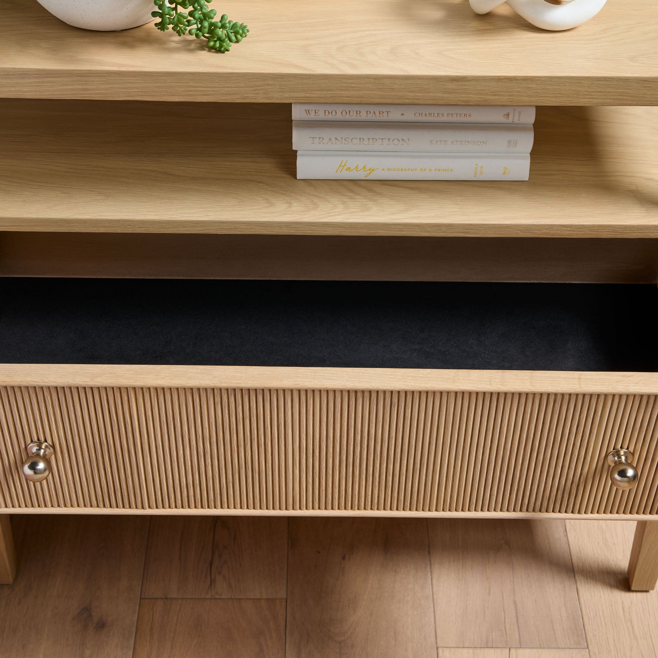 Open lower shelf with books and close-up of fluted wood drawer front and brass knobs on nightstand