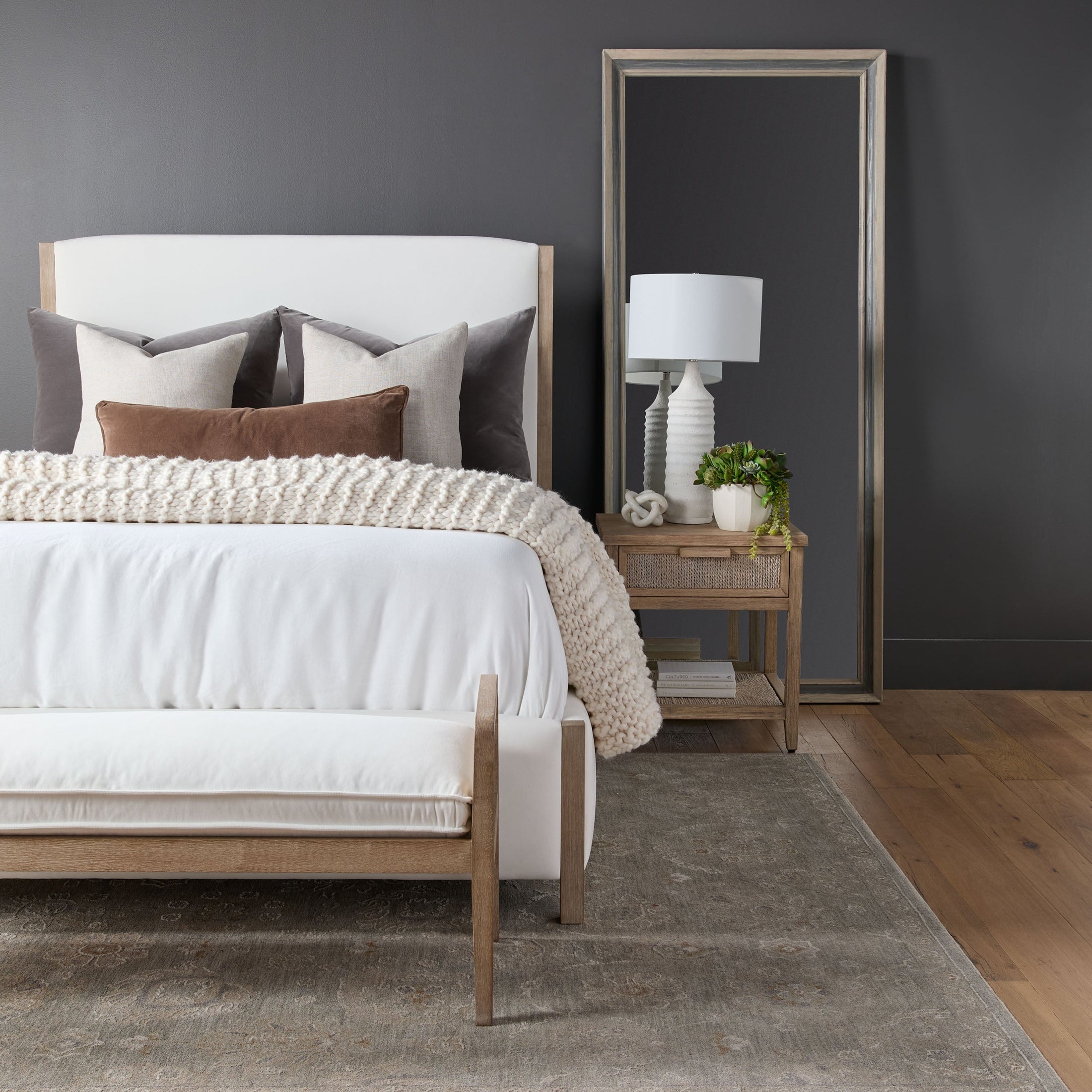Bedroom with neutral tones featuring a wooden bench with white upholstery at the foot of the bed