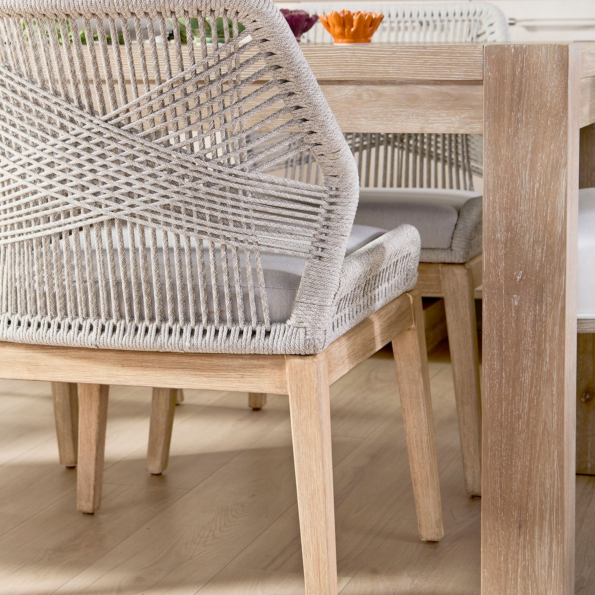 Close-up of a woven taupe and white rope dining chair with solid wood legs next to a light wood dining table