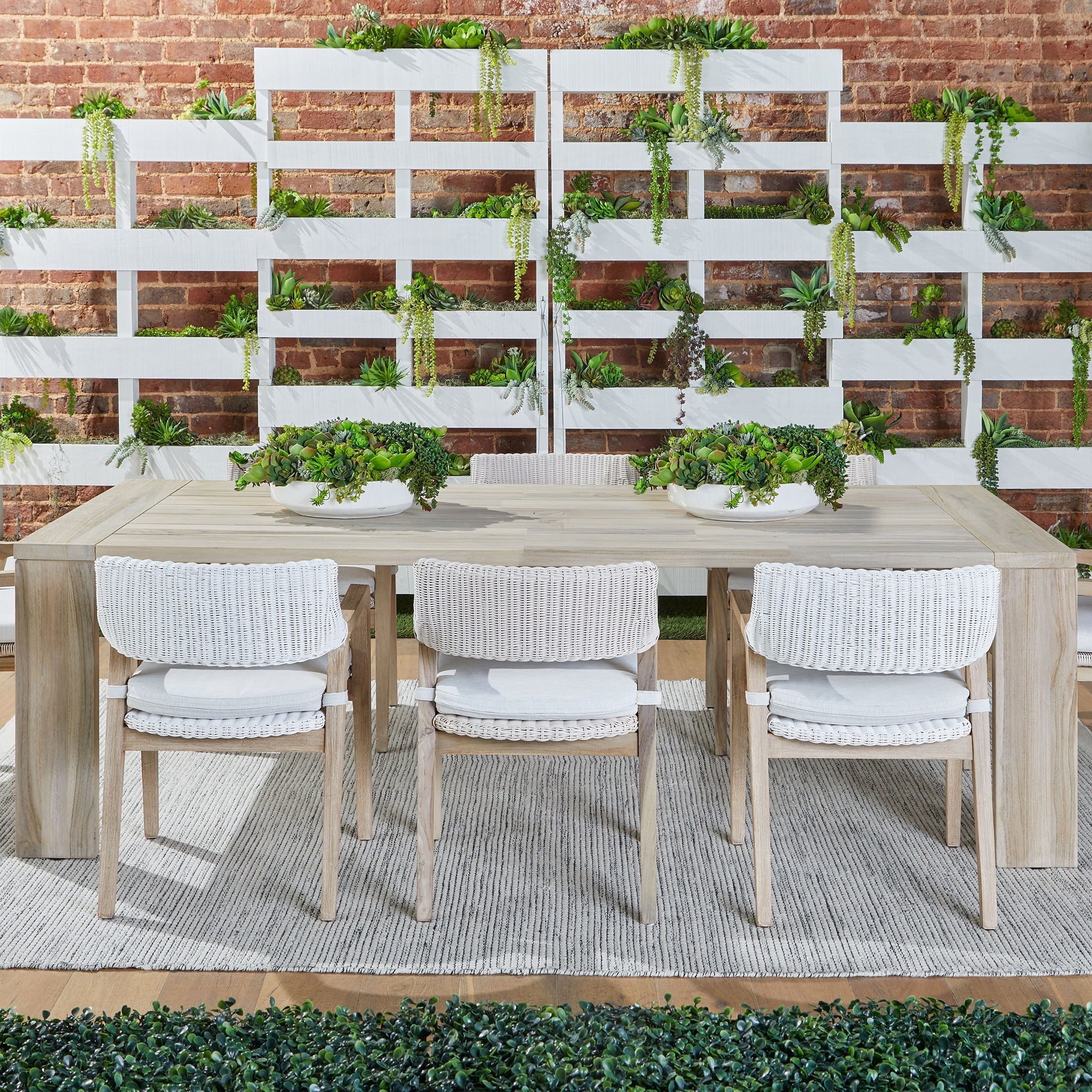 Three Lucia Outdoor Arm Chairs with white wicker and gray teak frames around a wooden dining table on a patio.