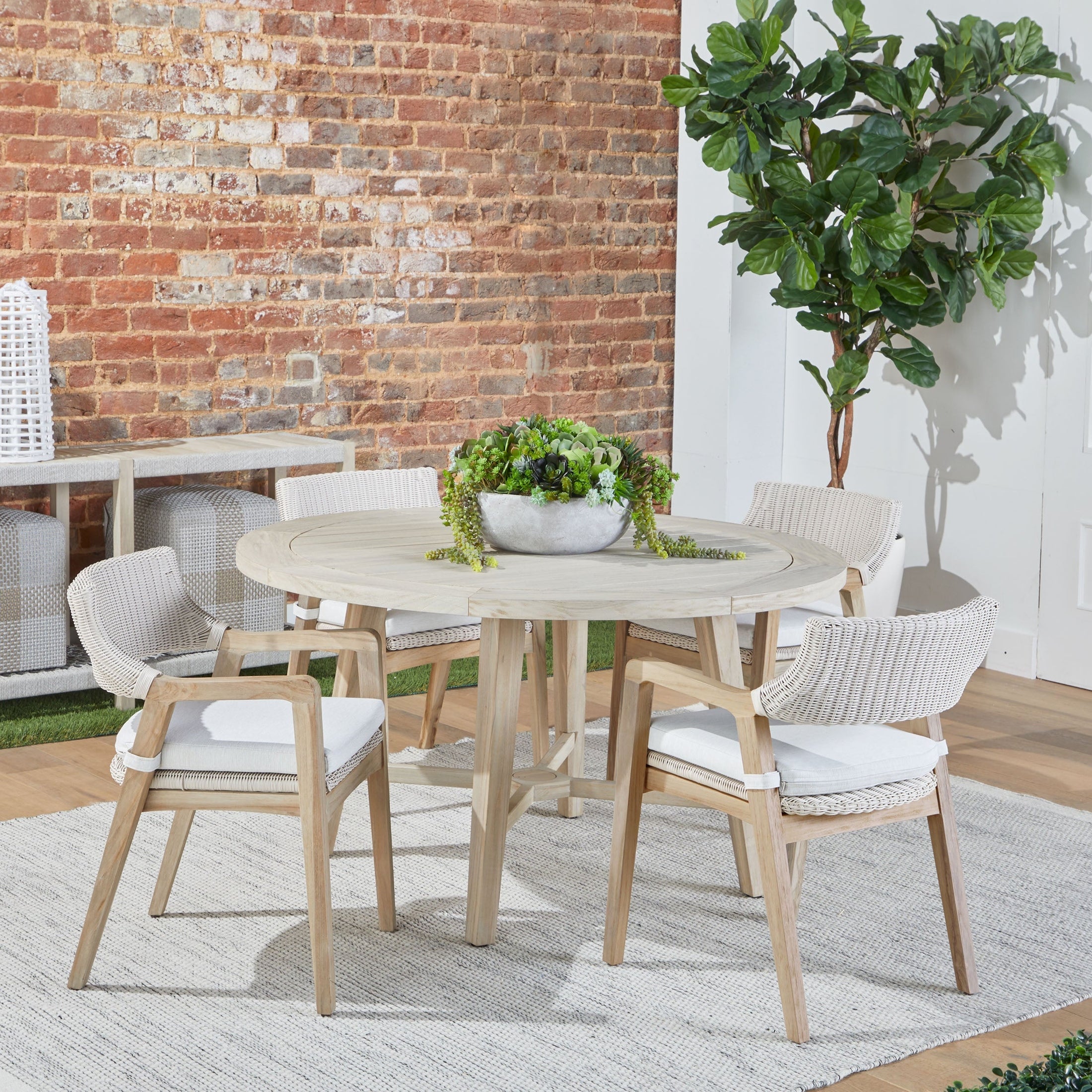 Essentials for Living Lucia Outdoor Arm Chairs in white wicker with gray teak frame around a round light wood table indoors.