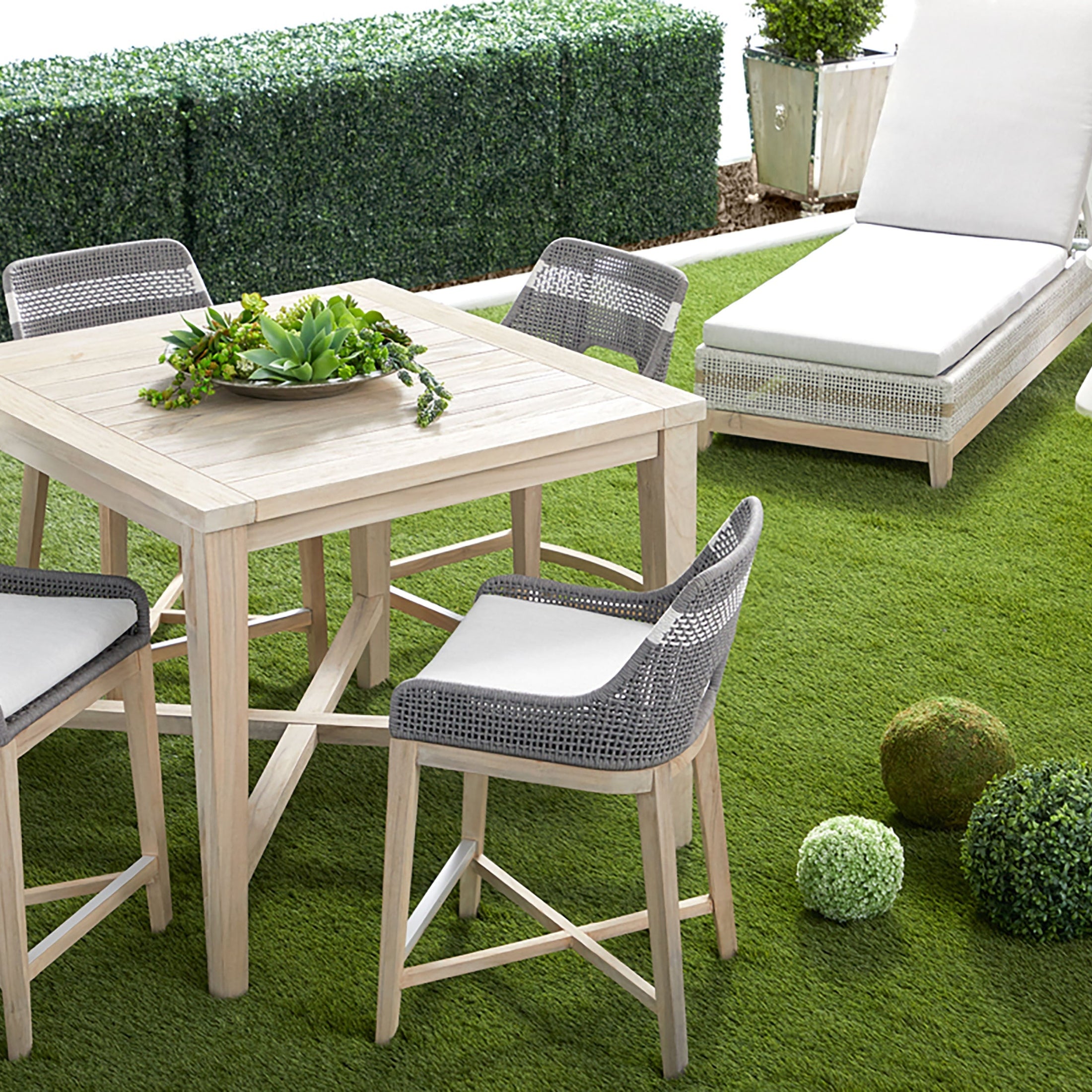 Outdoor patio setting with light wood table and woven chairs on green artificial grass lawn