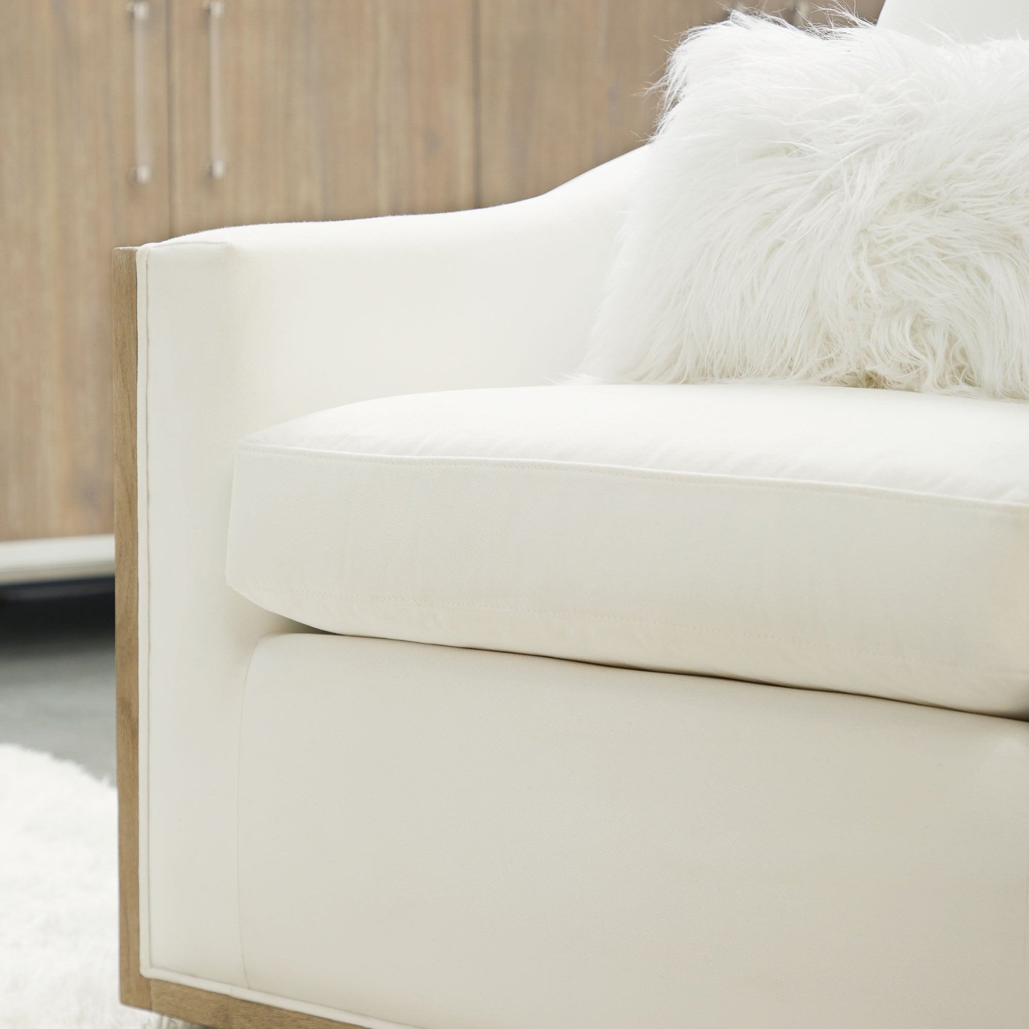 Close-up of a white Paxton Swivel Club Chair armrest and cushion with plush throw pillow in light interior setting