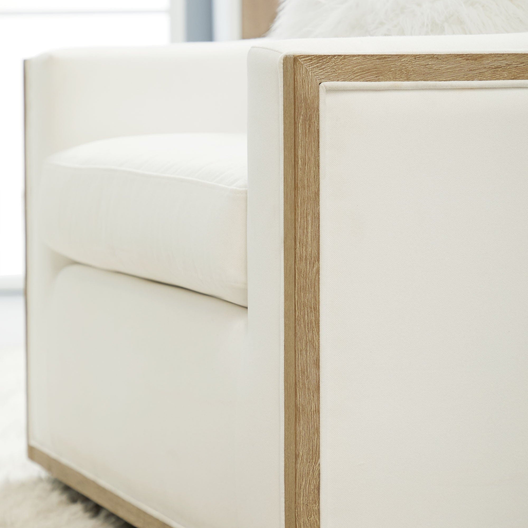 Close-up of Essentials For Living Paxton Swivel Club Chair showing natural gray oak trim and white upholstery detail