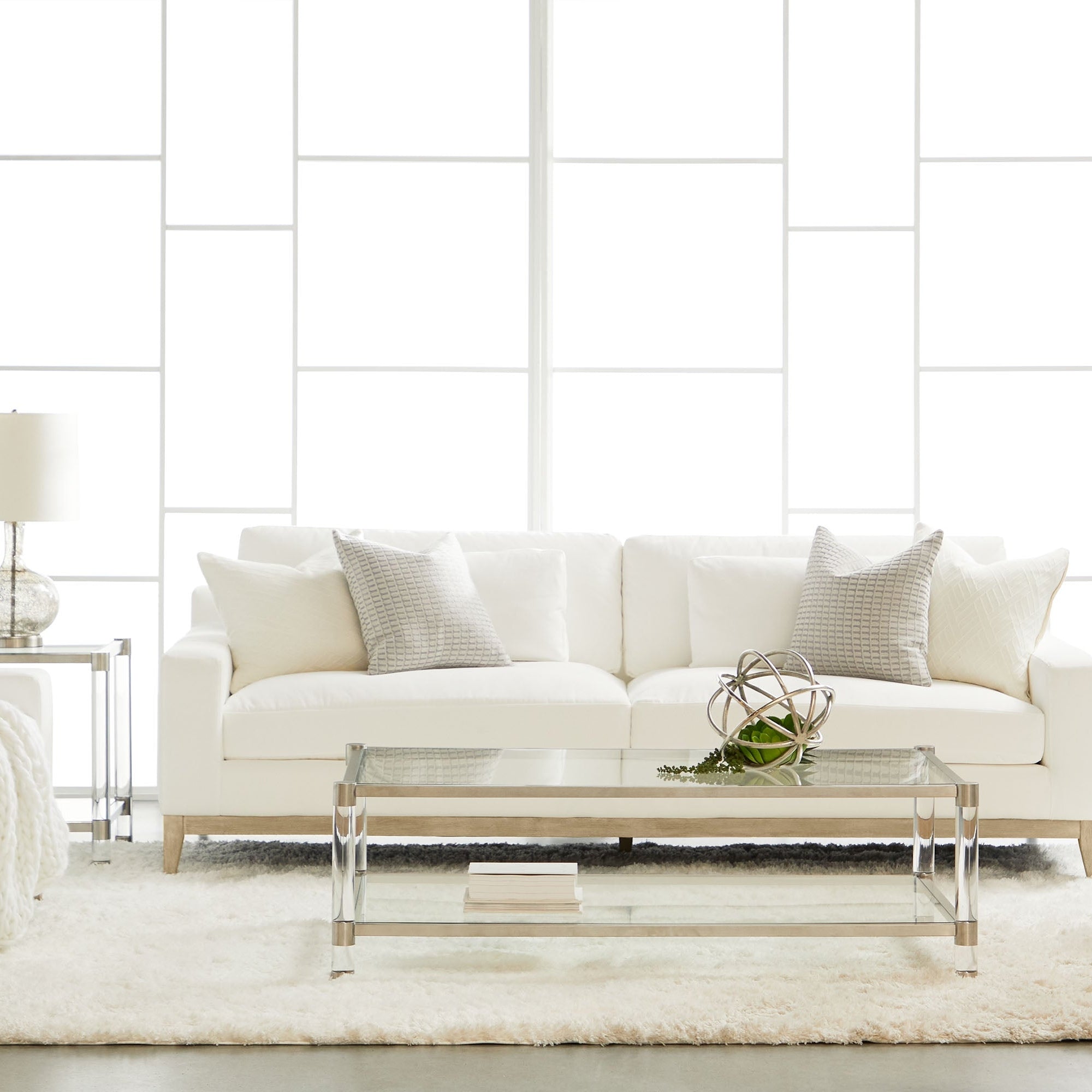 Modern white sofa with pale cushions in a bright room featuring glass coffee table and soft rug
