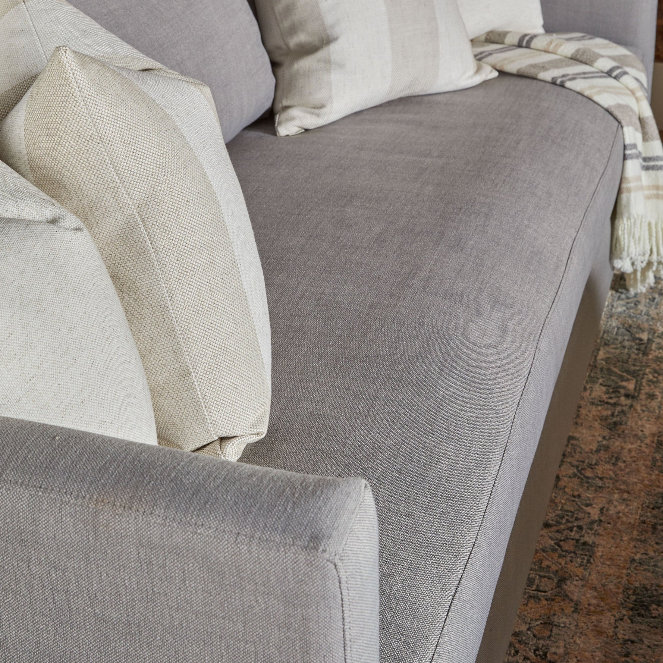 Close-up of a gray sofa with ivory and beige throw pillows and a striped throw blanket on a patterned rug