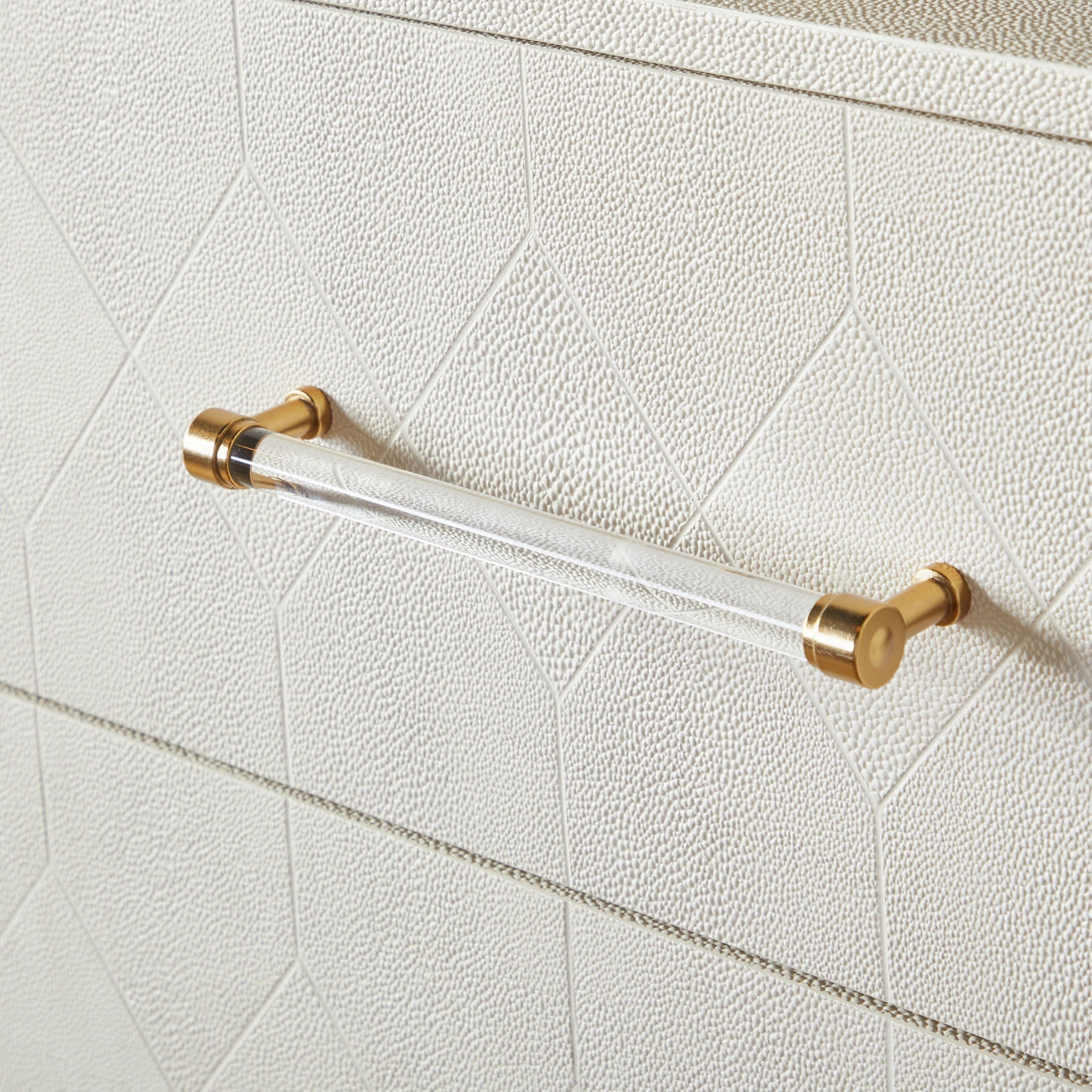 Close-up of pearl-white faux shagreen drawer front with clear acrylic handle and brushed brass accents on dresser