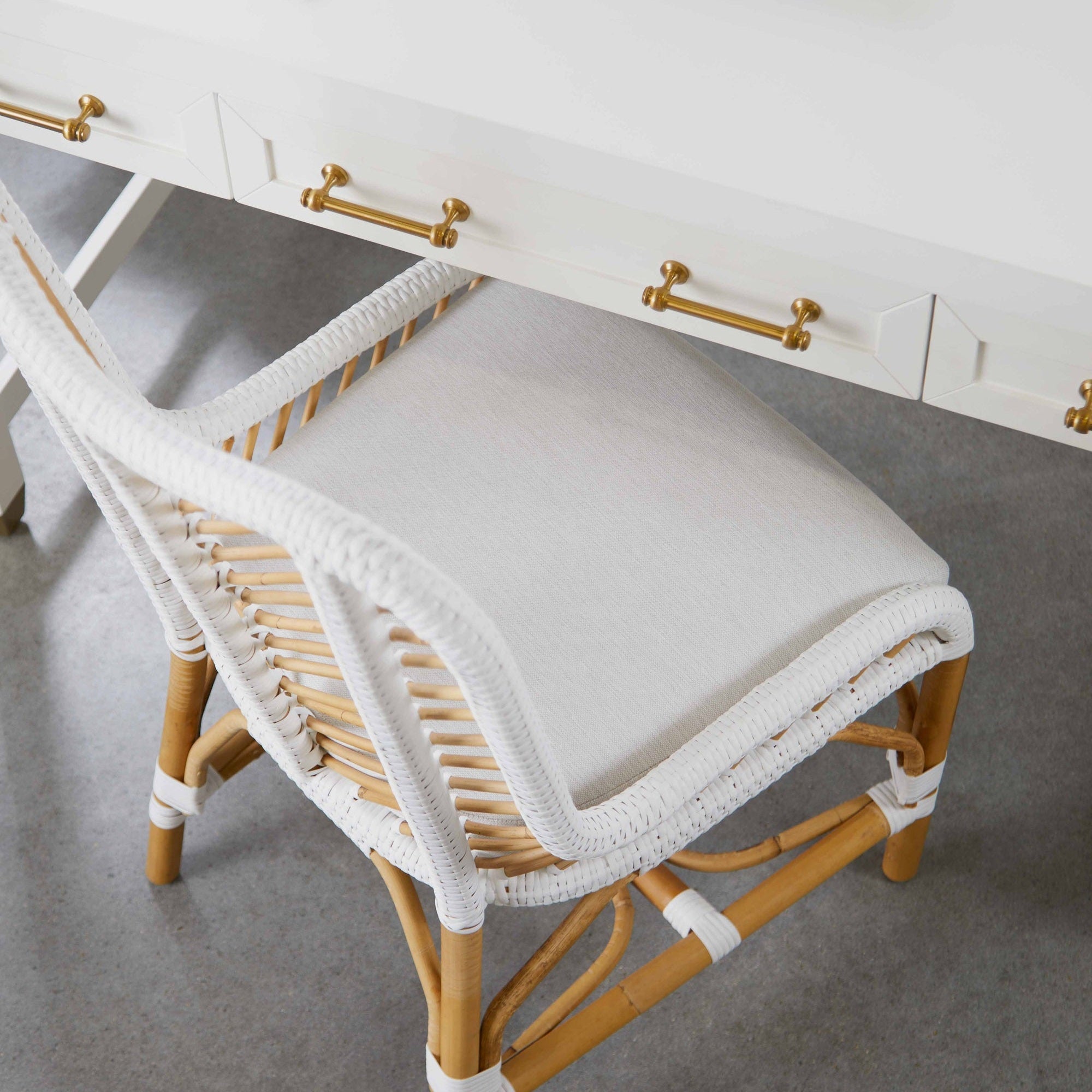 Close-up of a white lacquered Stella Desk with brushed brass handles paired with a woven rattan chair cushion seat