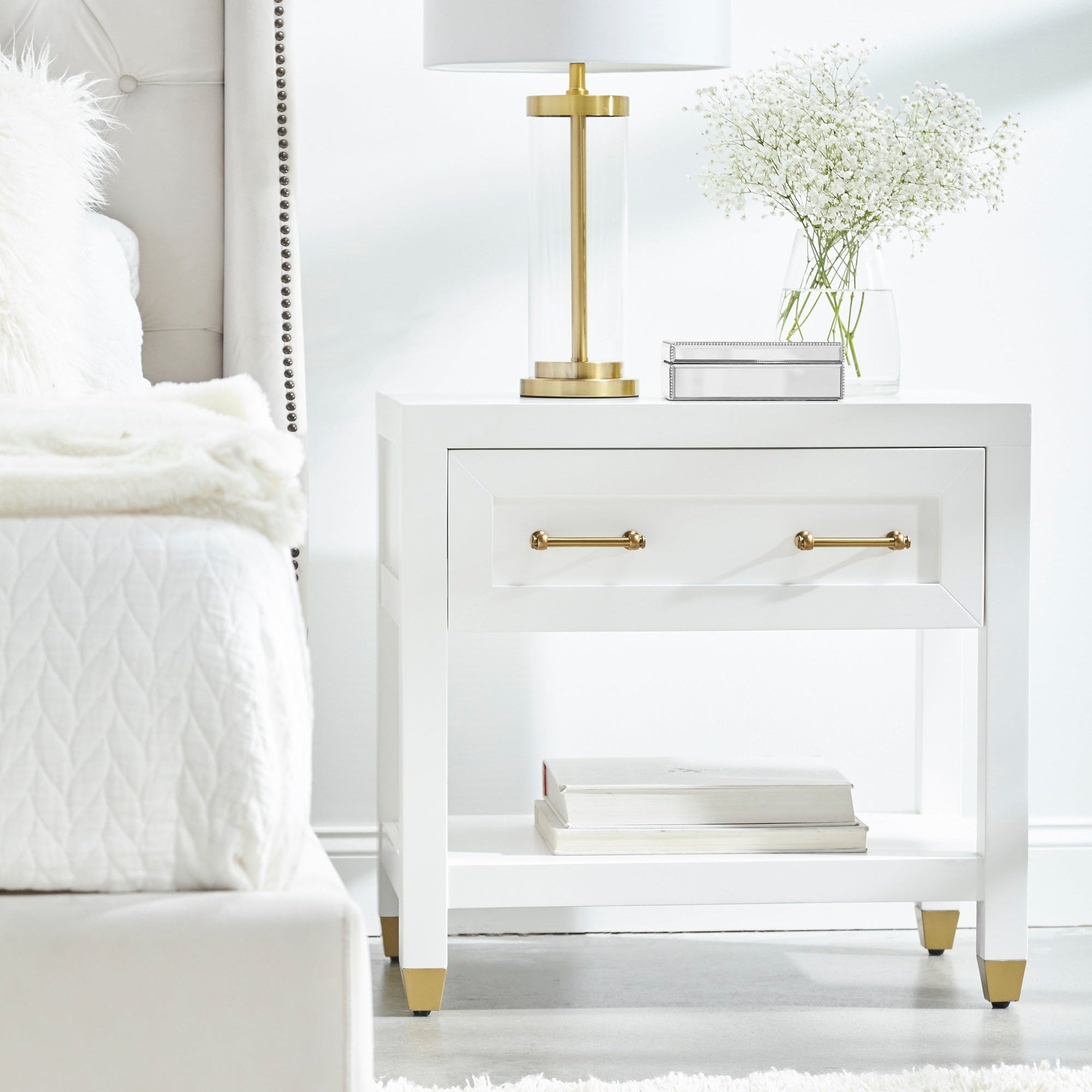 Essentials for Living Stella nightstand in matte white with brass handles and feet, featuring drawer and lower shelf storage.
