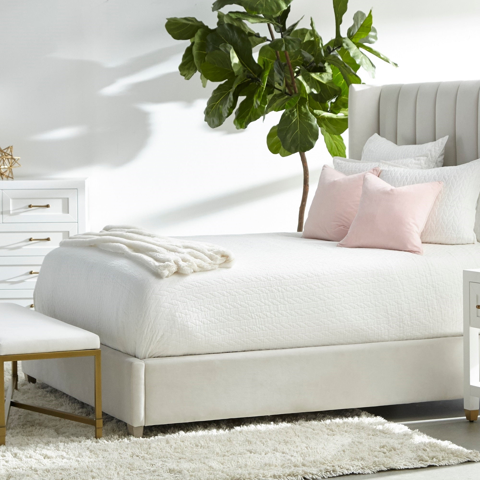 Essentials for Living Stella nightstand in matte white with brass hardware beside an upholstered bed with pink pillows