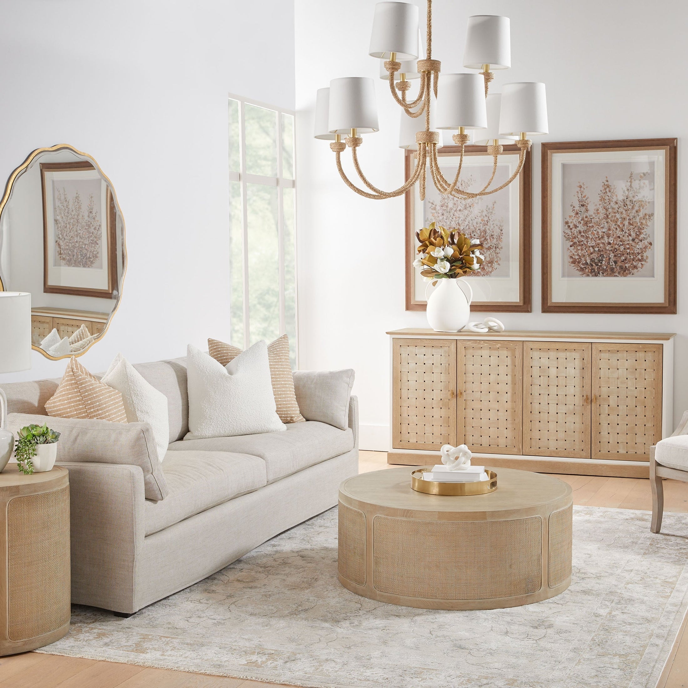 Bright modern living room with neutral sofa, round wood coffee table, rattan sideboard, and elegant chandelier