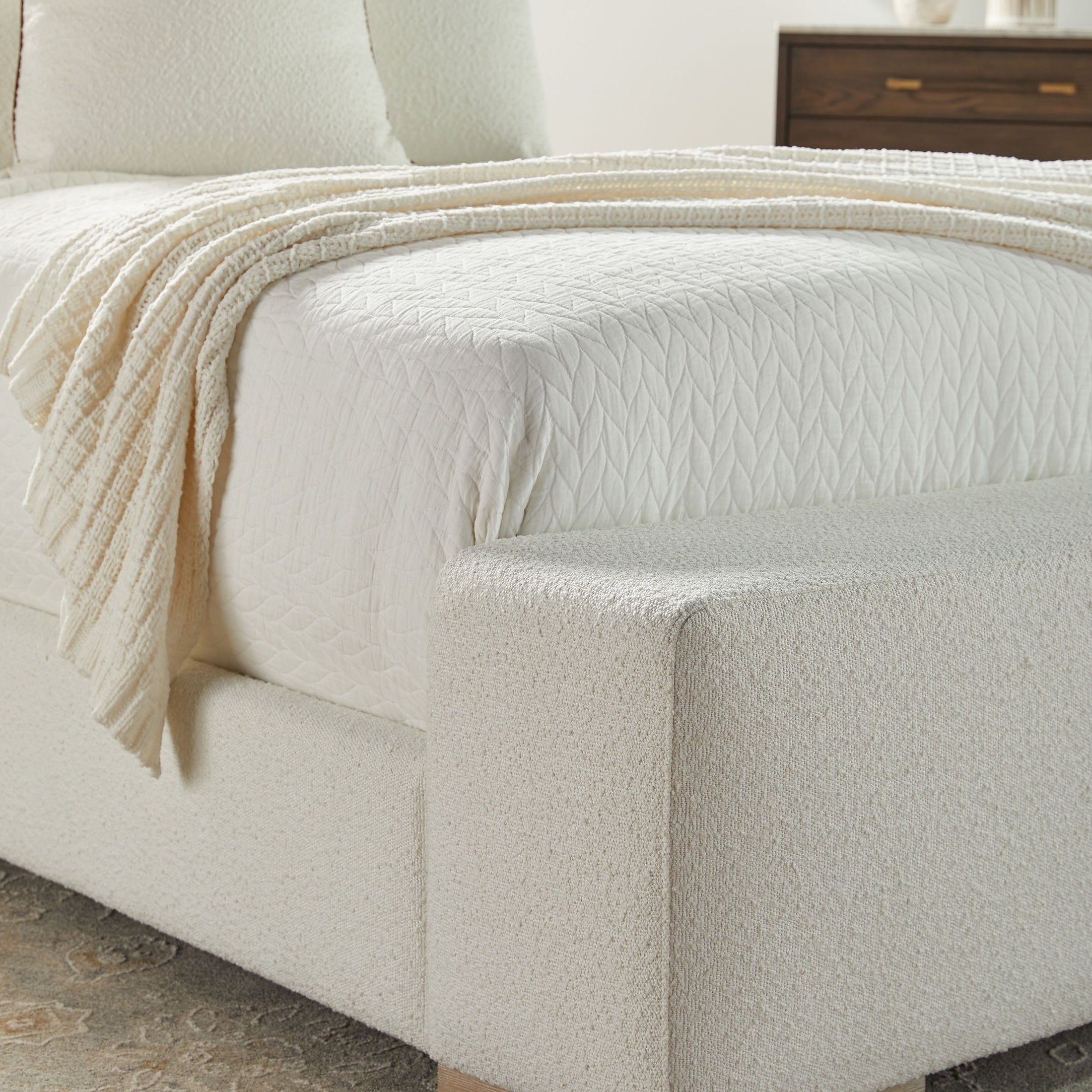 Close-up of the Warren Standard King Bed with white textured upholstery and a quilted mattress cover by Essentials For Living.