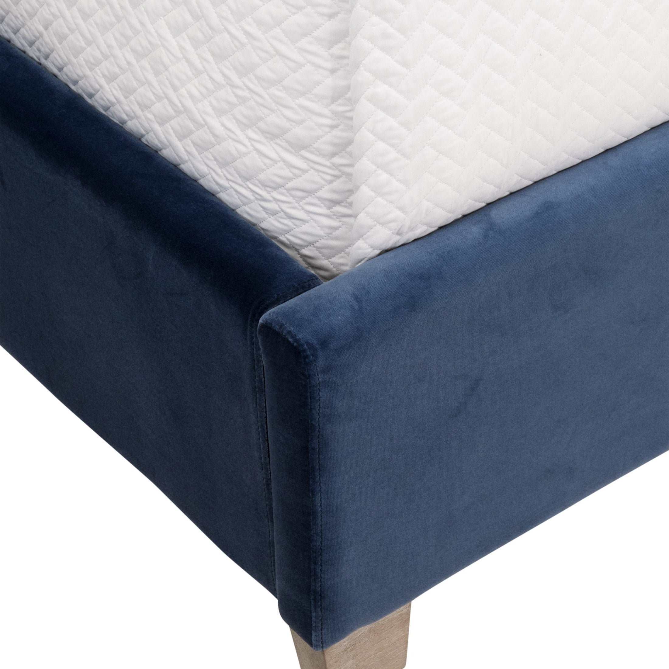 Close-up of blue velvet upholstered bed frame corner with solid oak leg and white quilted mattress cover