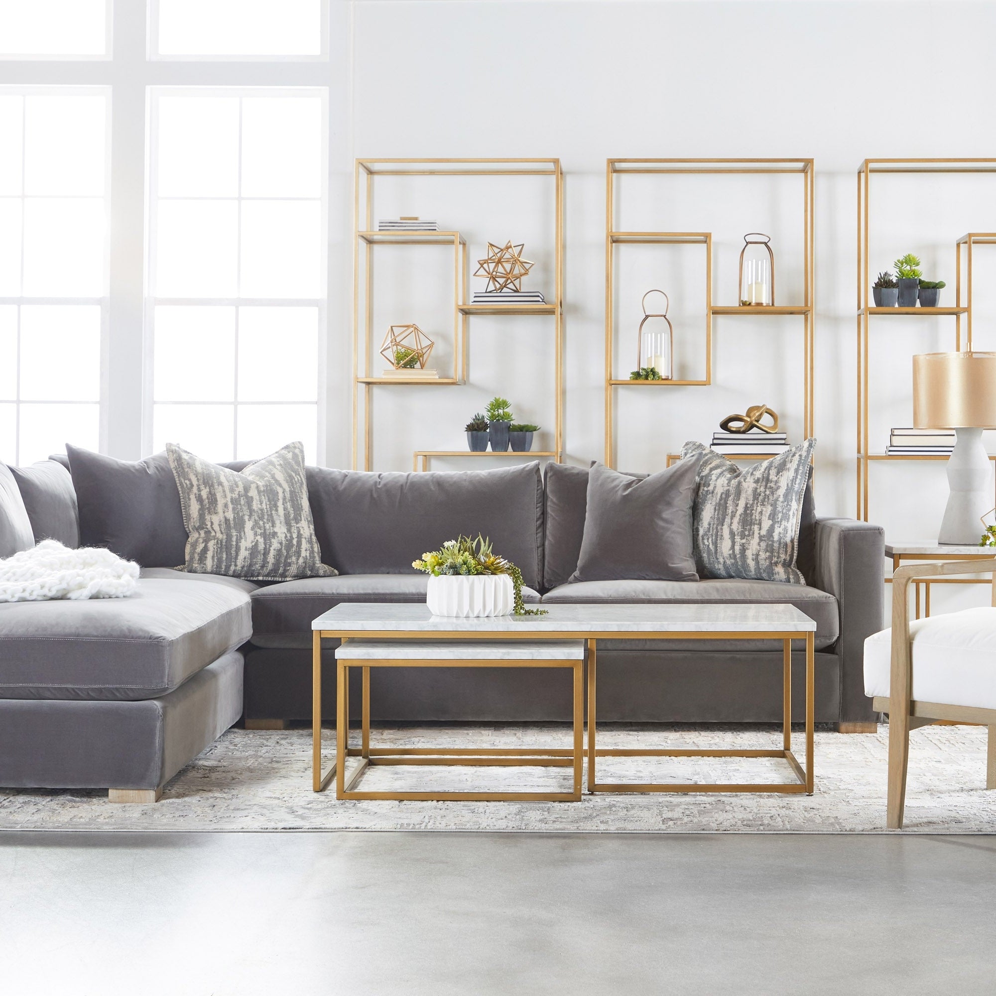 Modern living room with gray sectional sofa, gold geometric shelves, and nested marble-top coffee tables