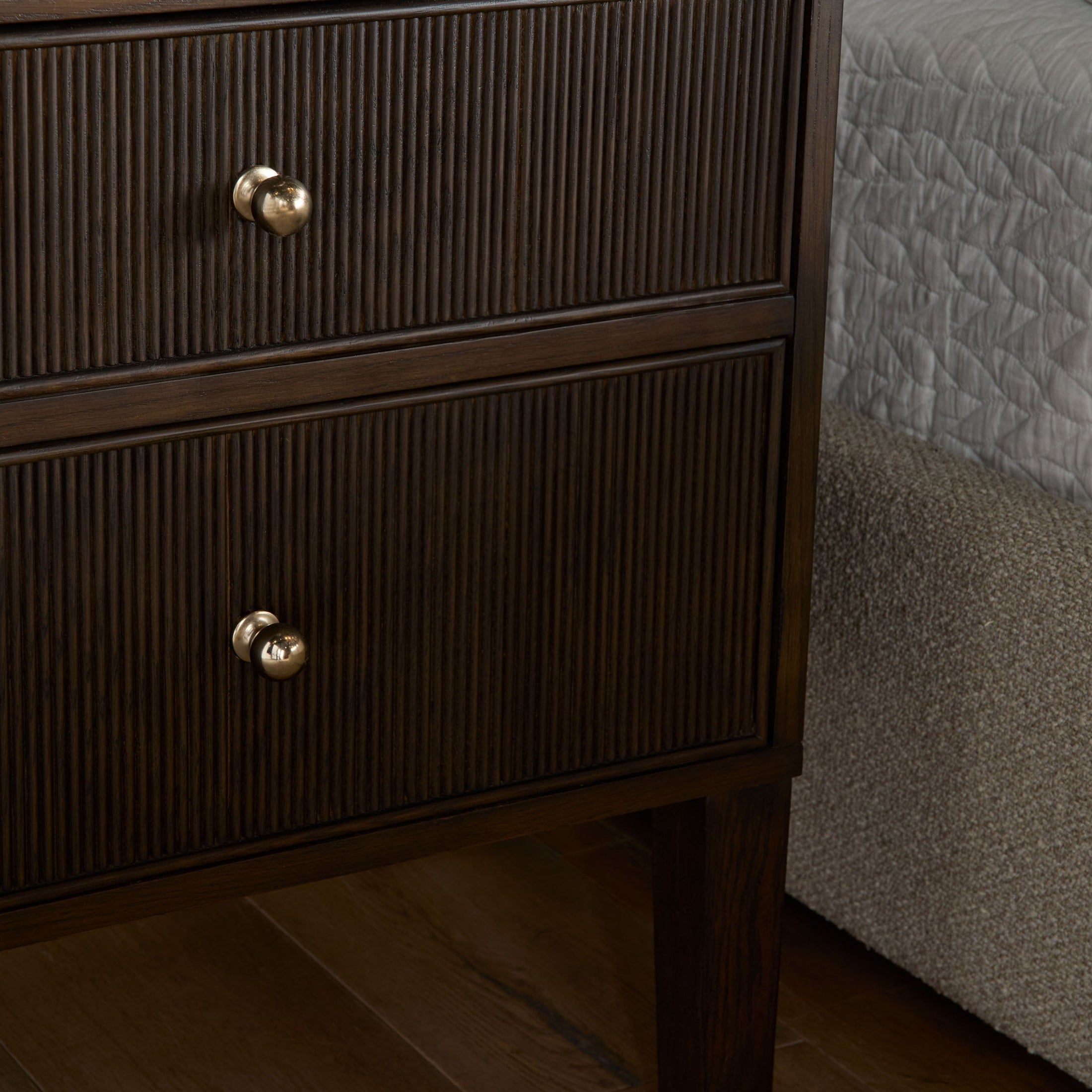 Dark oak 2-drawer nightstand with fluted detailing and brass knobs beside a bed with gray bedding