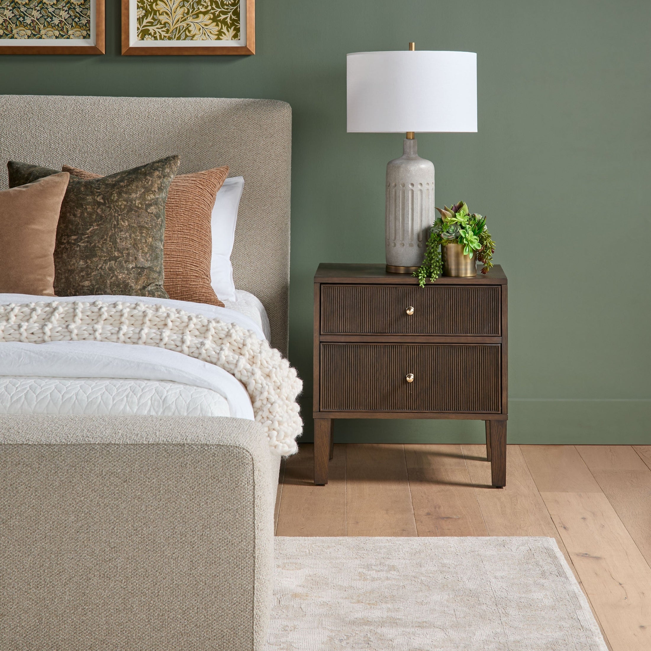 Highland 2-drawer nightstand in dark oak with fluted detailing, brass knobs, lamp, and greenery on top next to upholstered bed