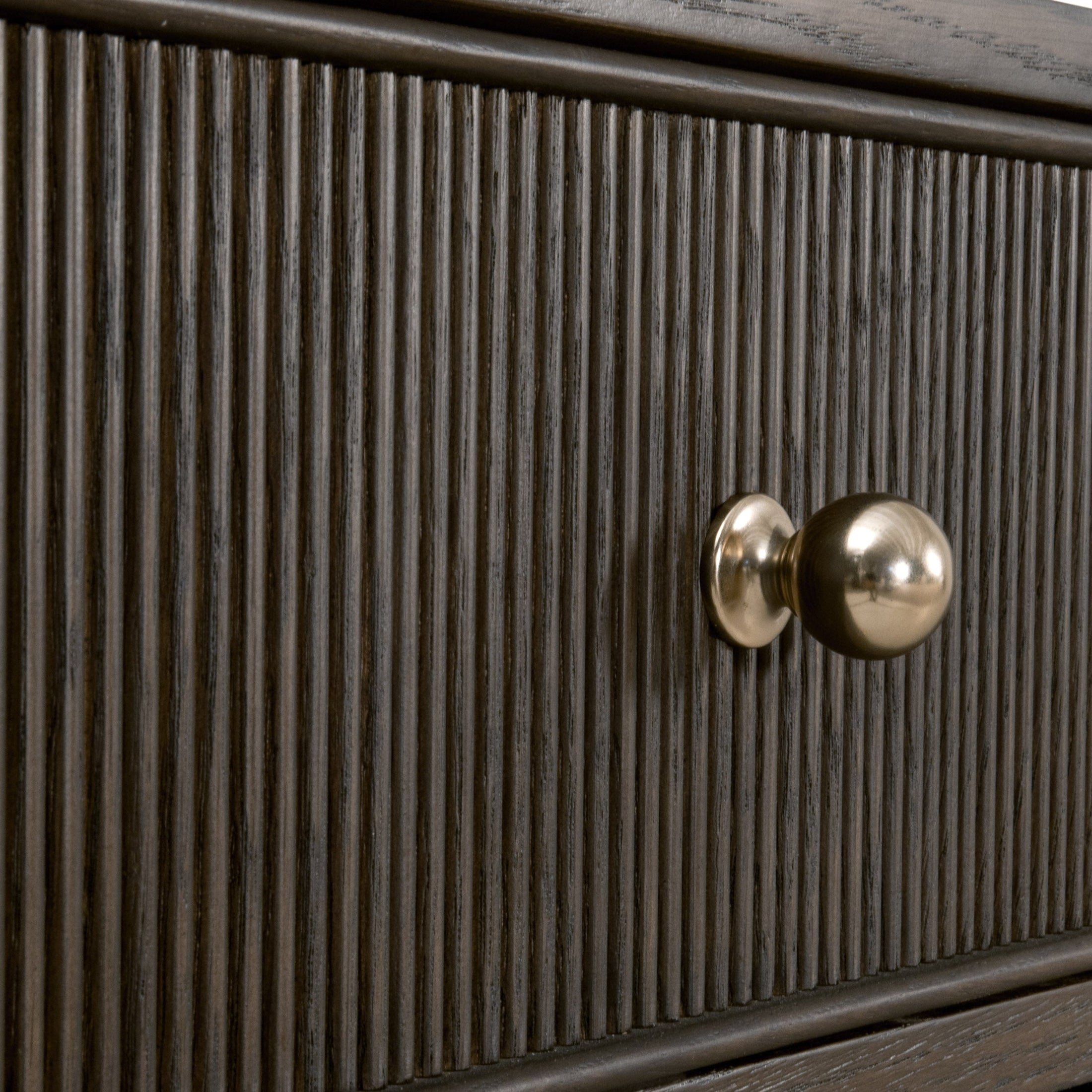 Close-up of fluted wood drawer front with polished brass finished iron knob on dark oak dresser drawer