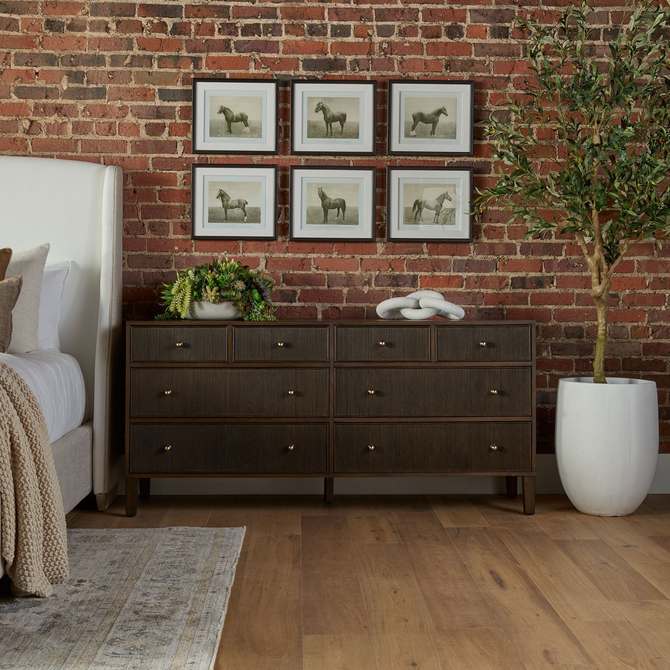 Dark brown 8-drawer dresser with brass knobs in a stylish bedroom setting with brick wall and framed artwork.