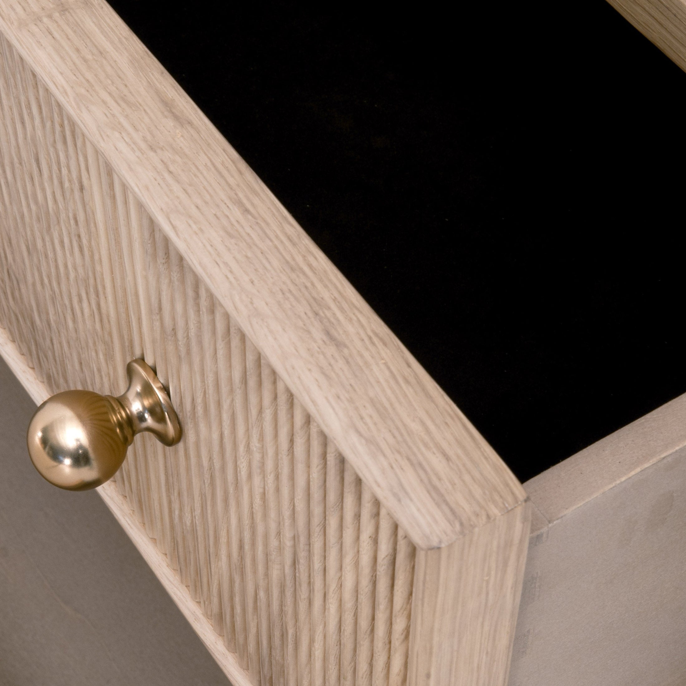 Close-up of open fluted wood drawer with polished brass knob and felt lining in a solid oak nightstand drawer