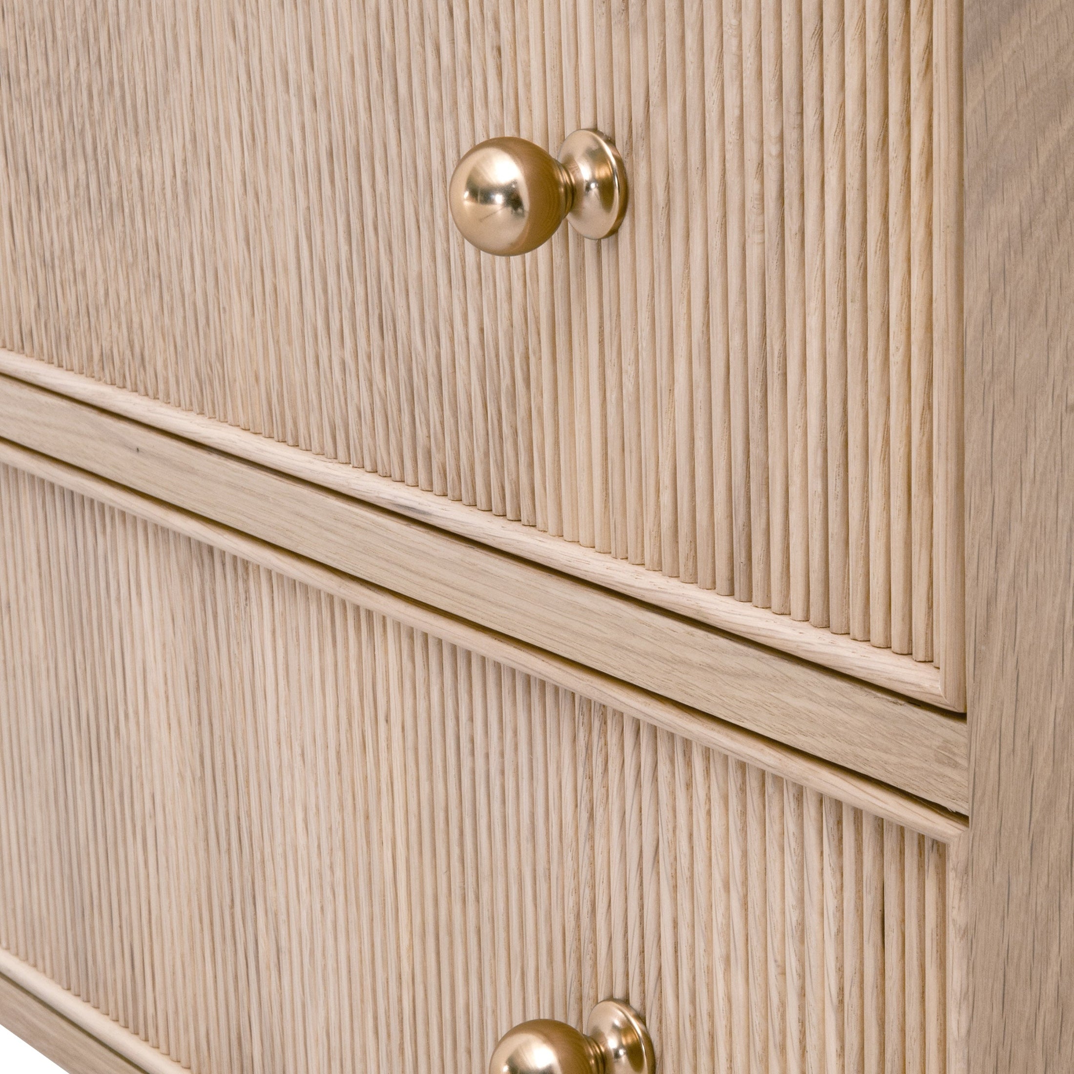 Close-up of fluted wood drawer fronts with polished brass knobs on a light oak nightstand.