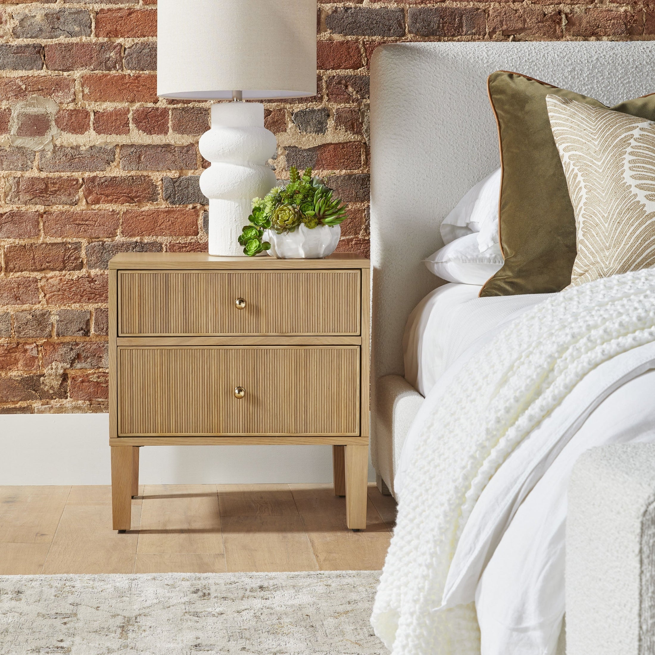 Highland 2-drawer nightstand in natural oak finish with brass knobs, next to bed with white bedding and green pillows