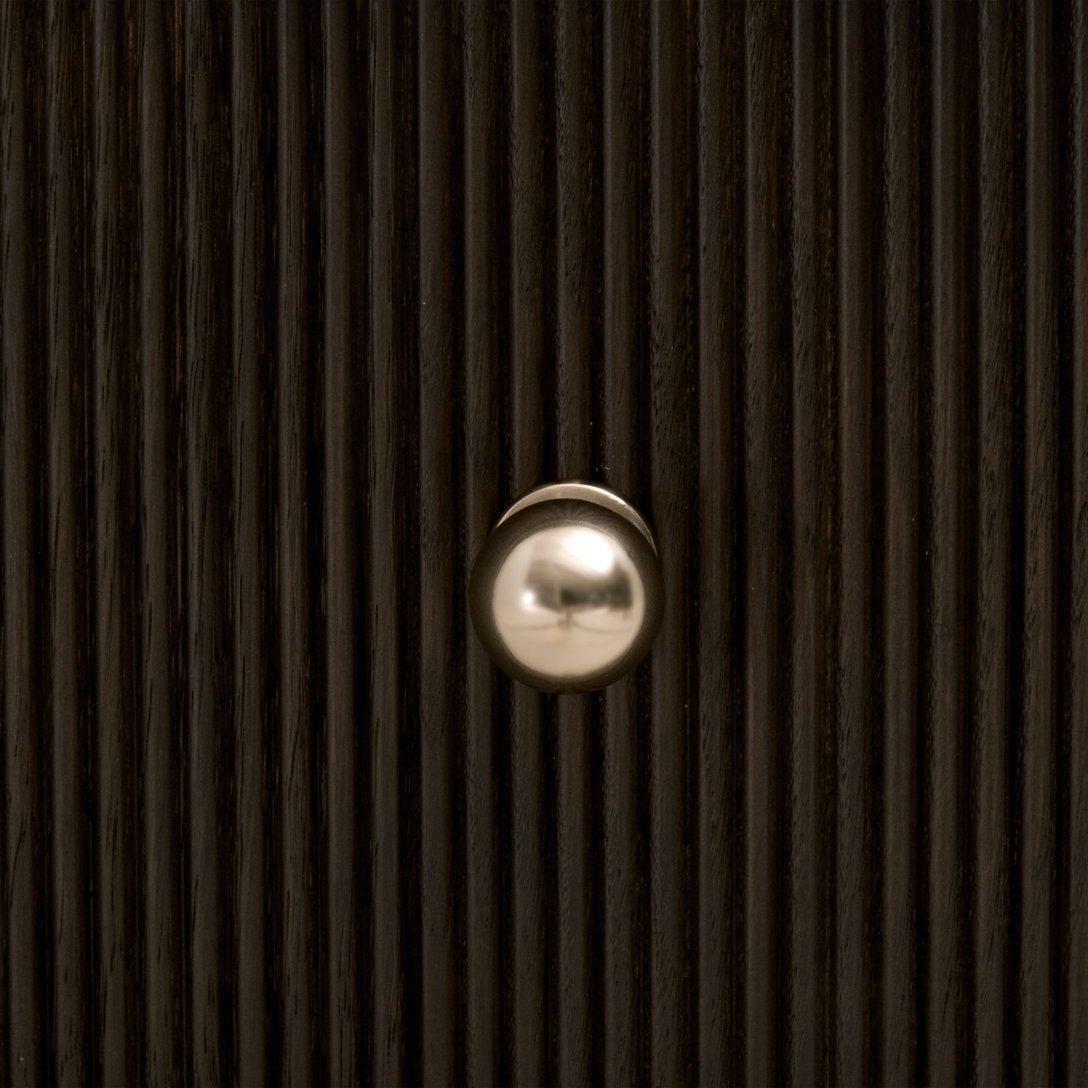 Close-up of polished brass knob on fluted dark oak wood drawer front from Essentials For Living nightstand