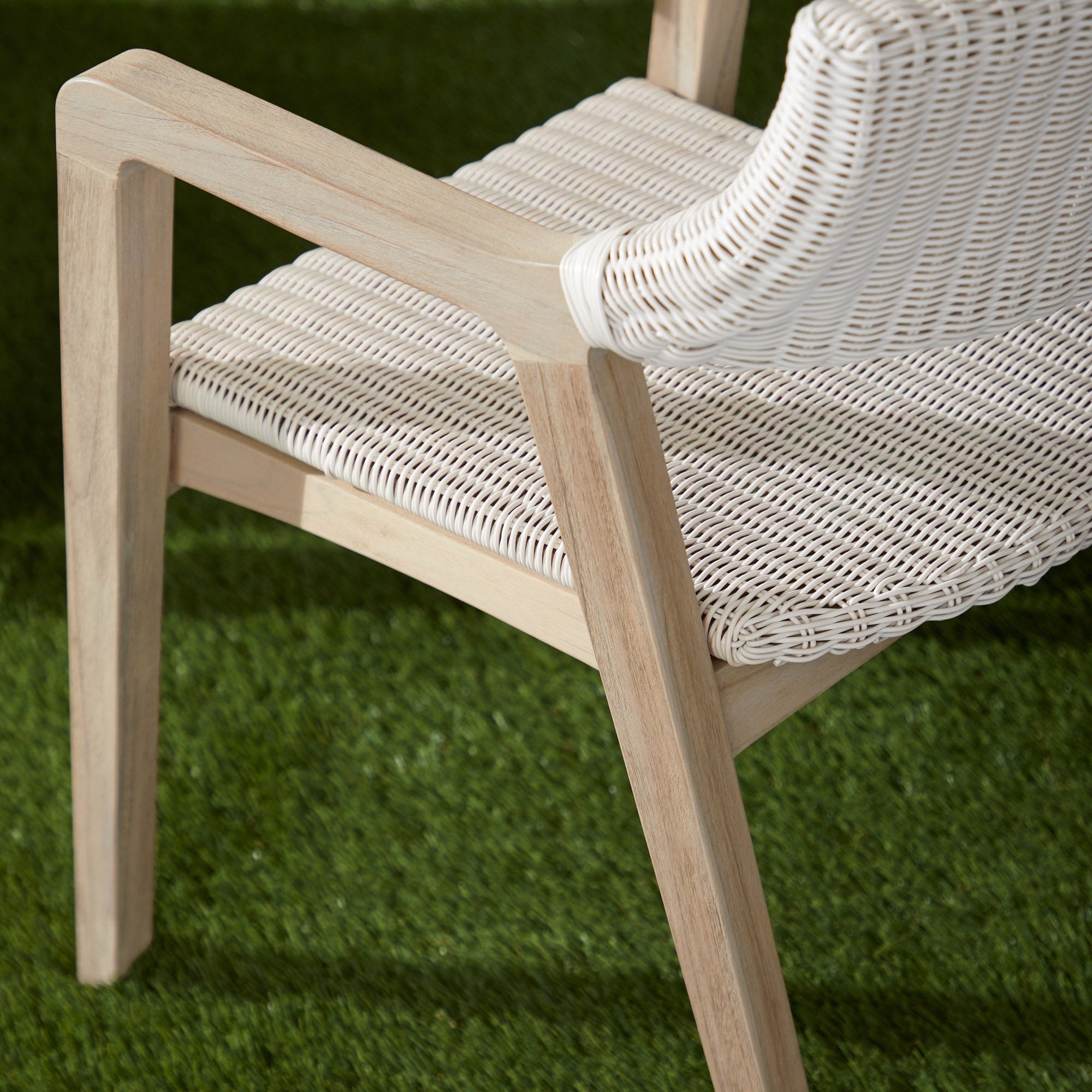 Close-up of Lucia Outdoor Arm Chair showing white wicker seat and gray teak wood armrest on green grass