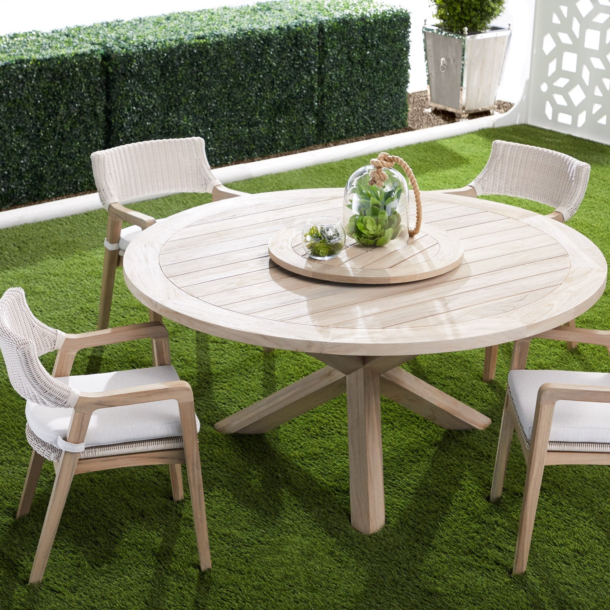 Set of four Lucia Outdoor Arm Chairs with white wicker and gray teak frames around a round wooden dining table on green grass.