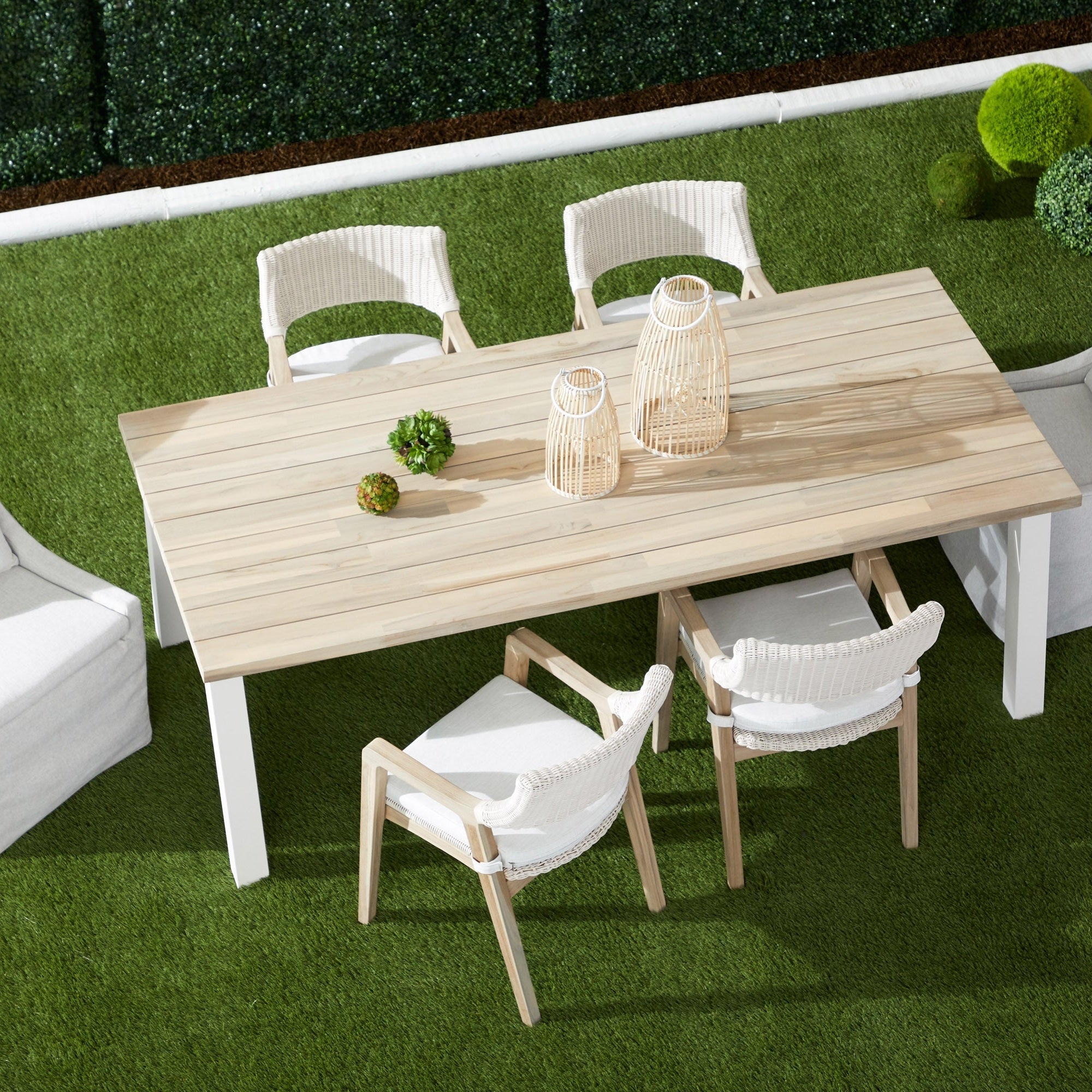 Outdoor dining set with white wicker Lucia arm chairs and light wood table on green grass lawn