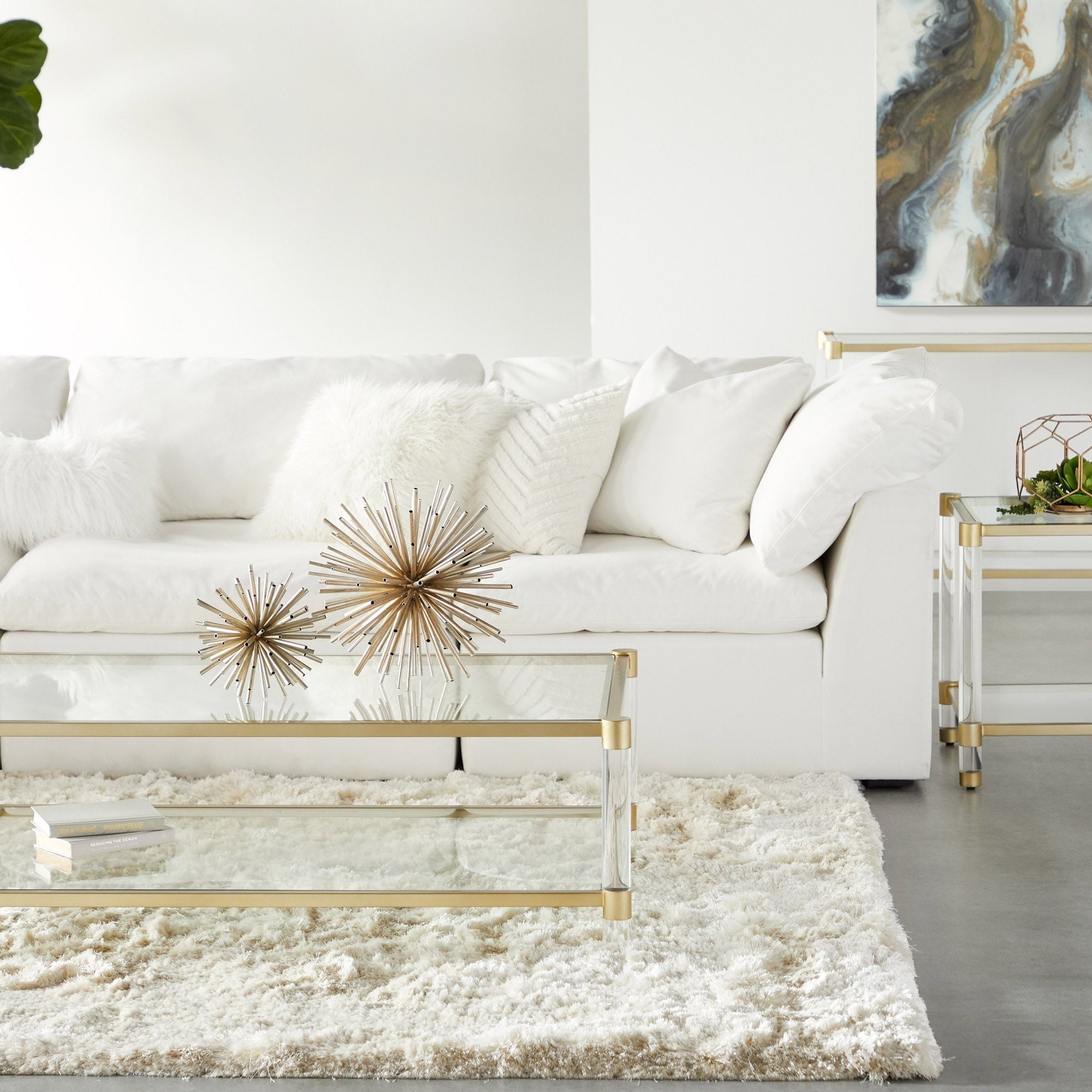 Nouveau Console Table with brushed brass frame, clear glass shelves, and Lucite legs in stylish living room by Essentials for Living.