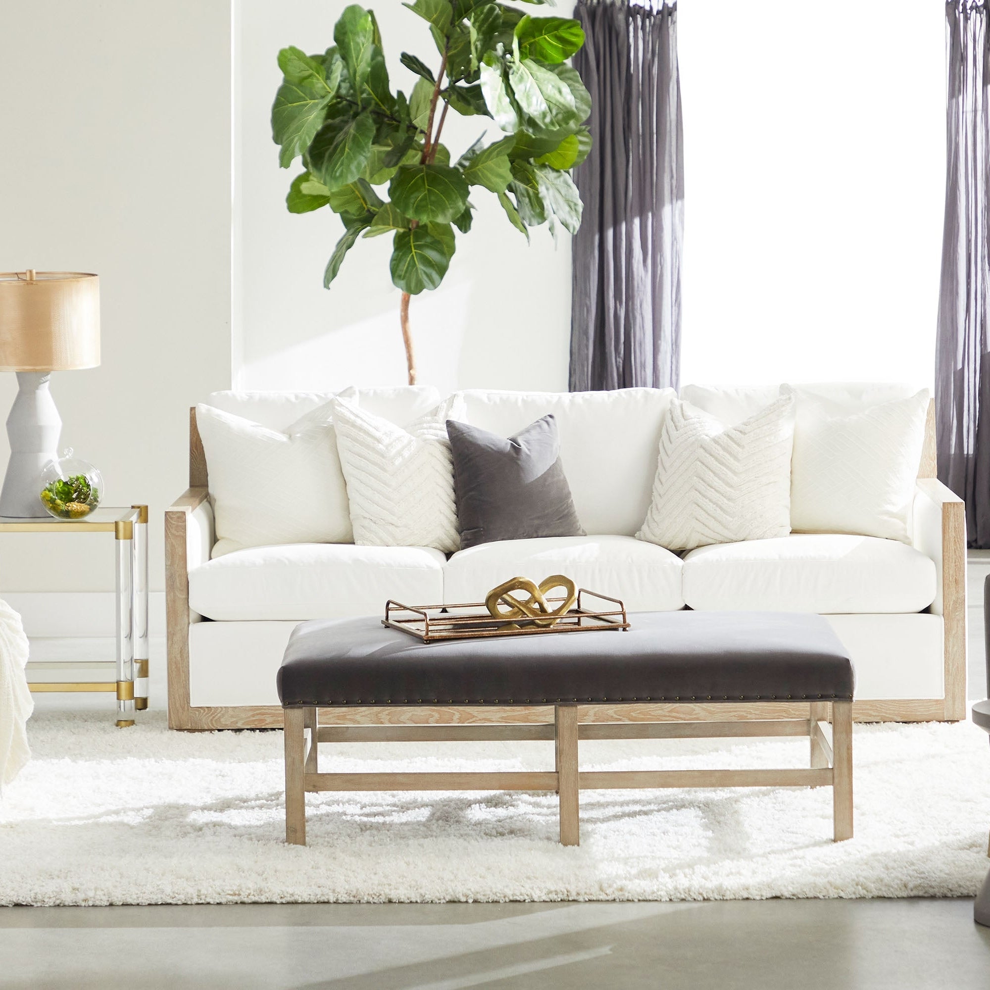 Nouveau End Table with brushed brass frame, clear glass shelves, and lucite legs in a bright living room by Essentials for Living