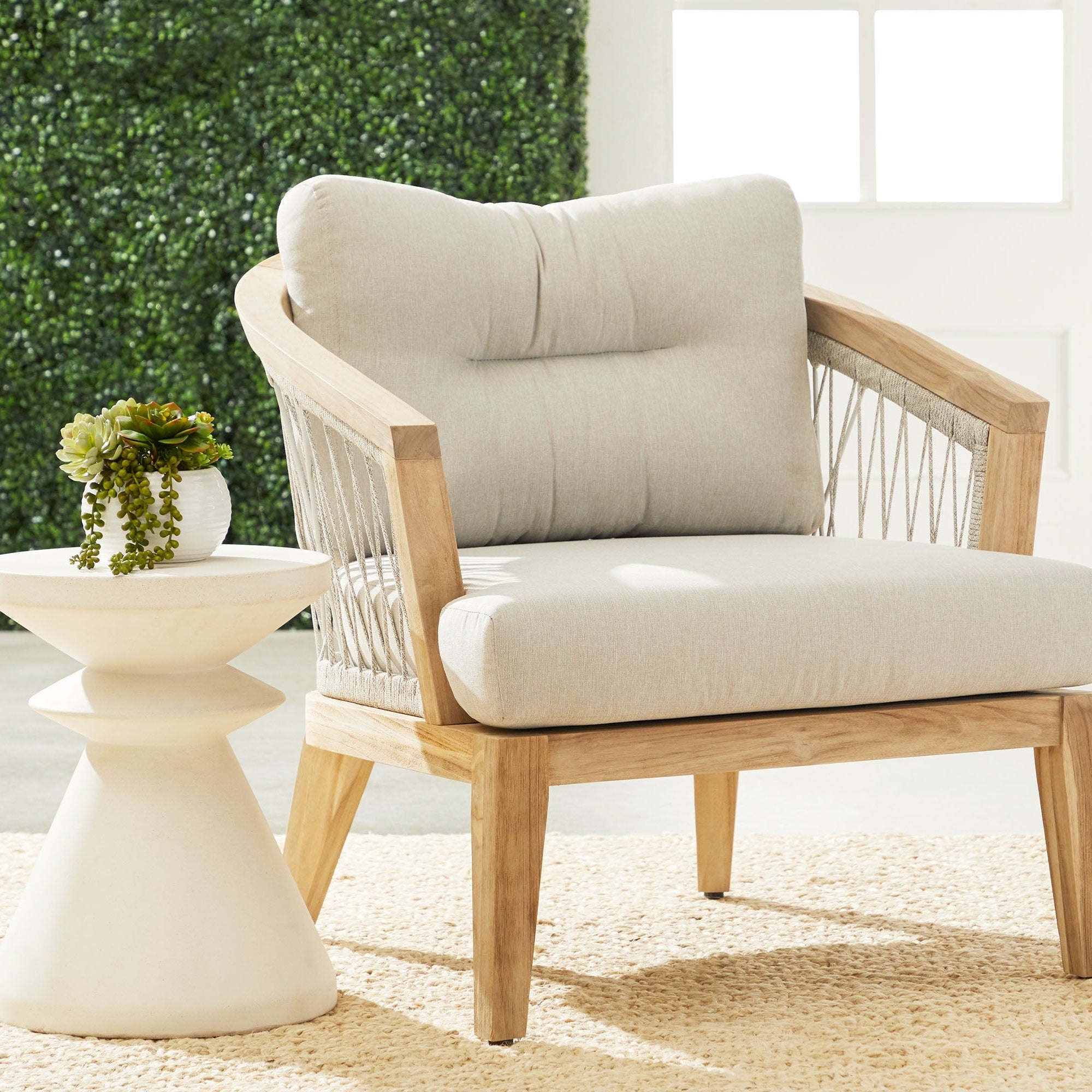Ivory sculptural Pawn Accent Table by Essentials for Living next to a cushioned wooden lounge chair with greenery backdrop