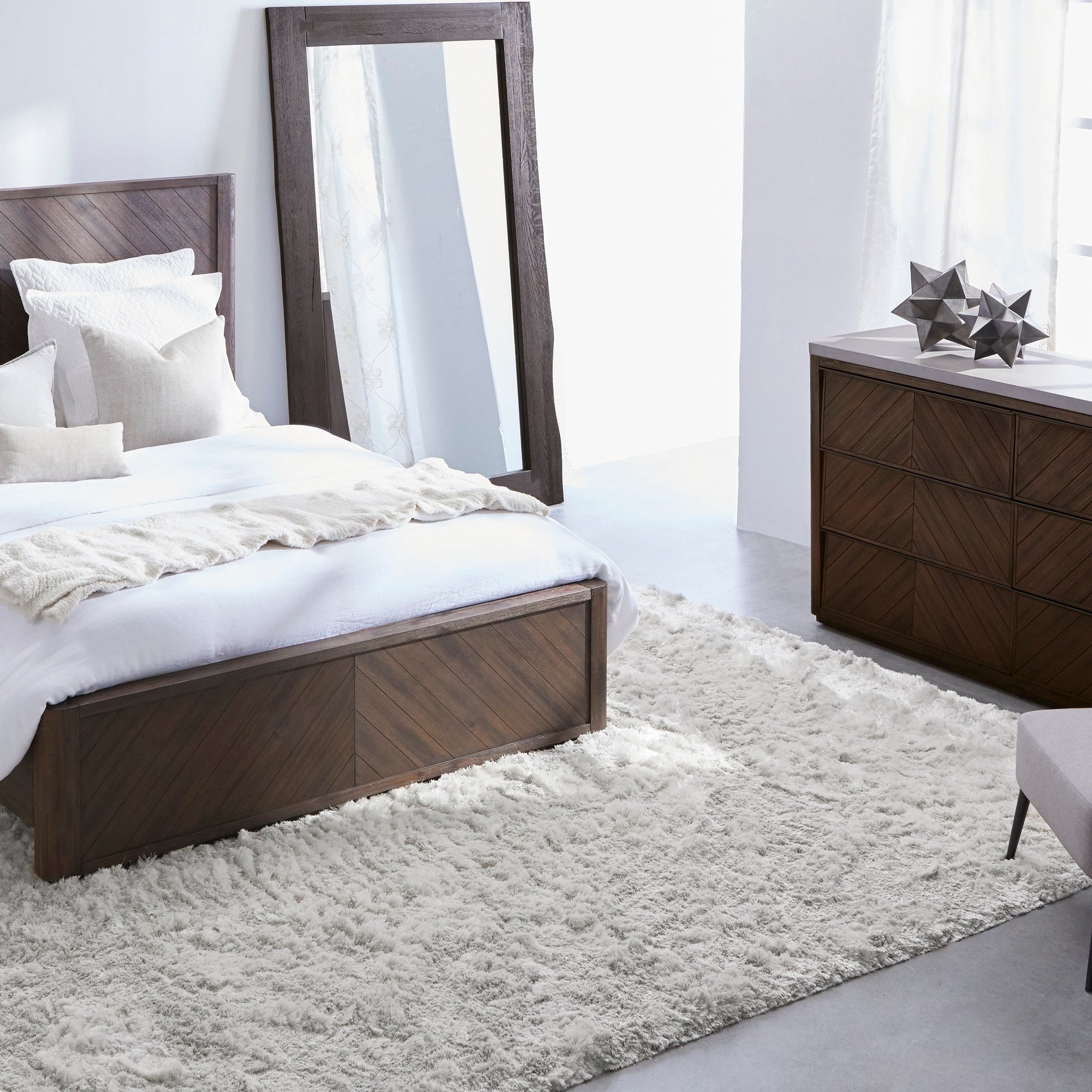 Light-filled modern bedroom with wood furniture, fluffy white rug, and large floor mirror by window