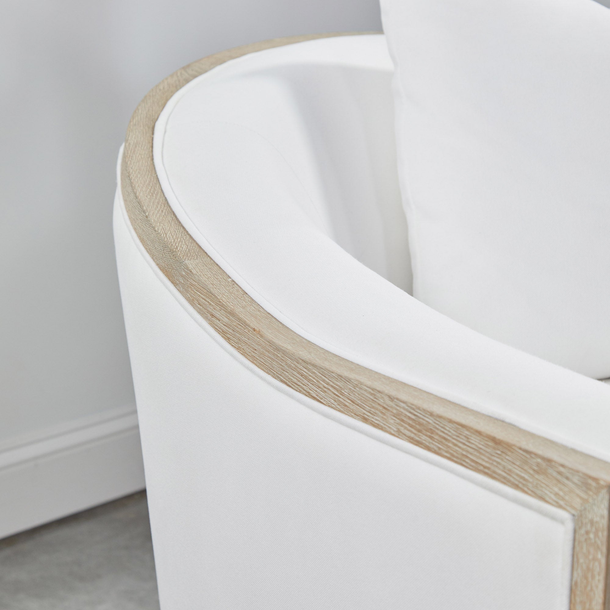Close-up of the Paxton Swivel Club Chair's barrel shape with natural gray oak trim and white upholstery by Essentials For Living