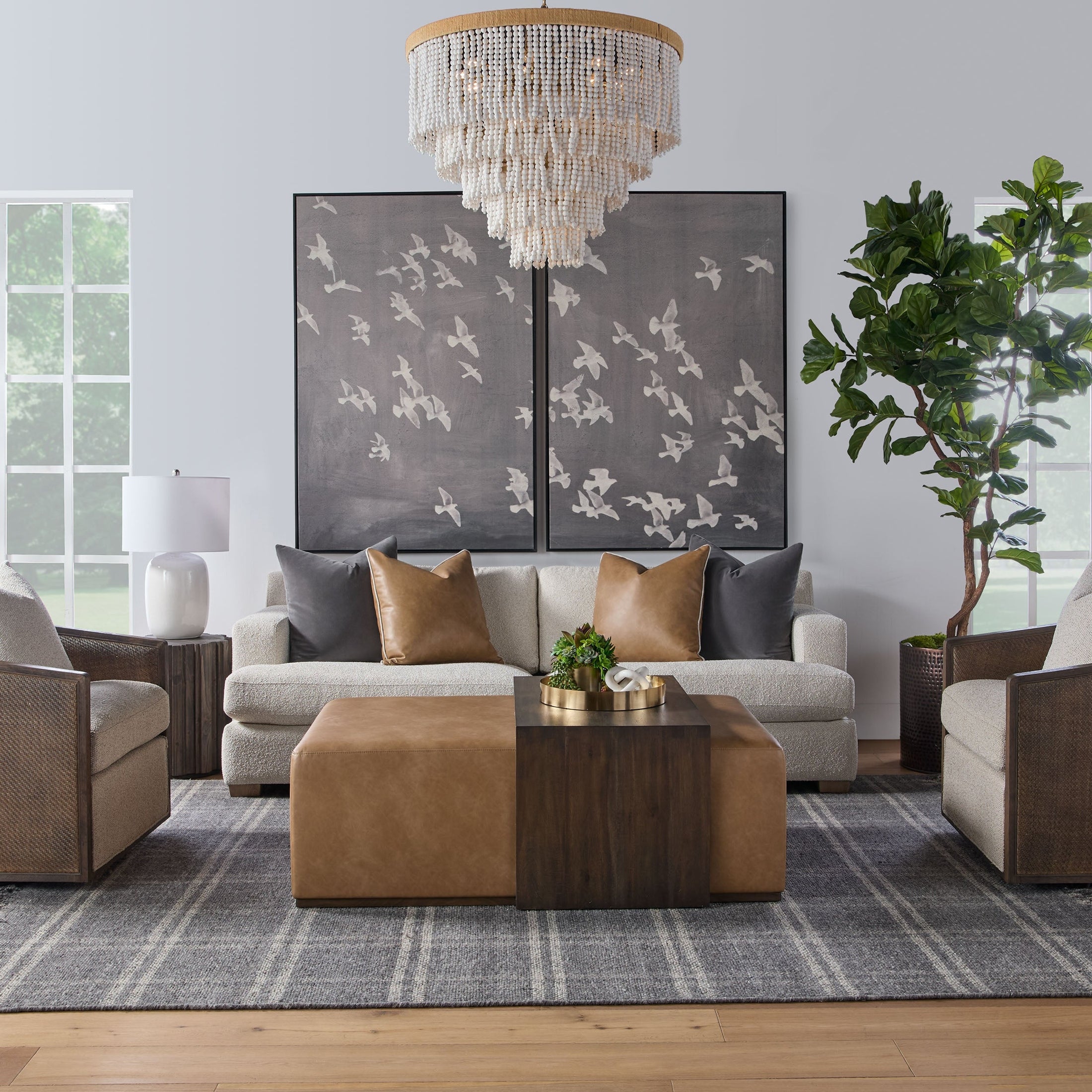 Elegant living room featuring a neutral sofa with accent pillows, a leather ottoman, dark wood table, and large bird artwork wall decor