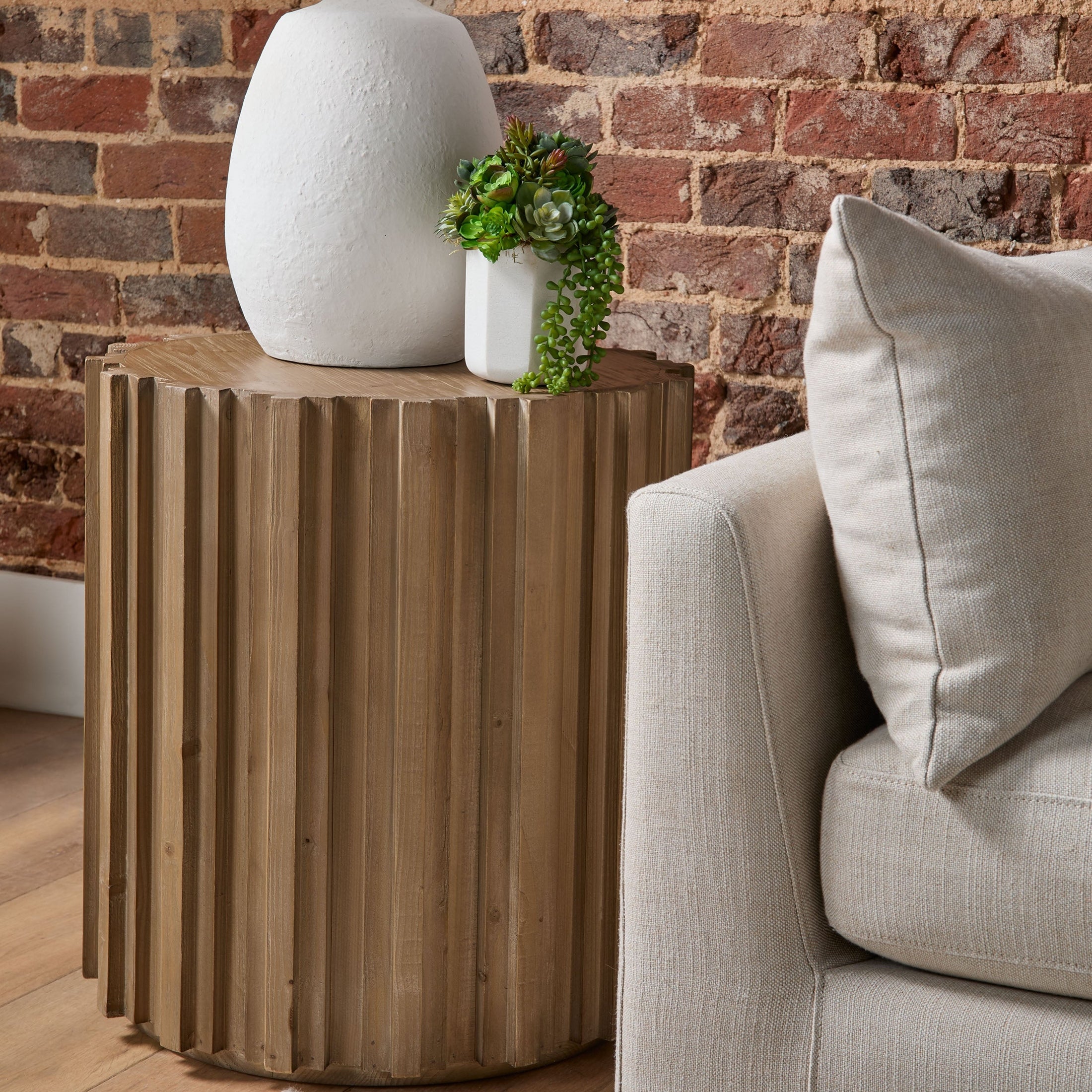 Round wooden Roma End Table by Essentials for Living with fluted sides beside beige sofa in cozy living room