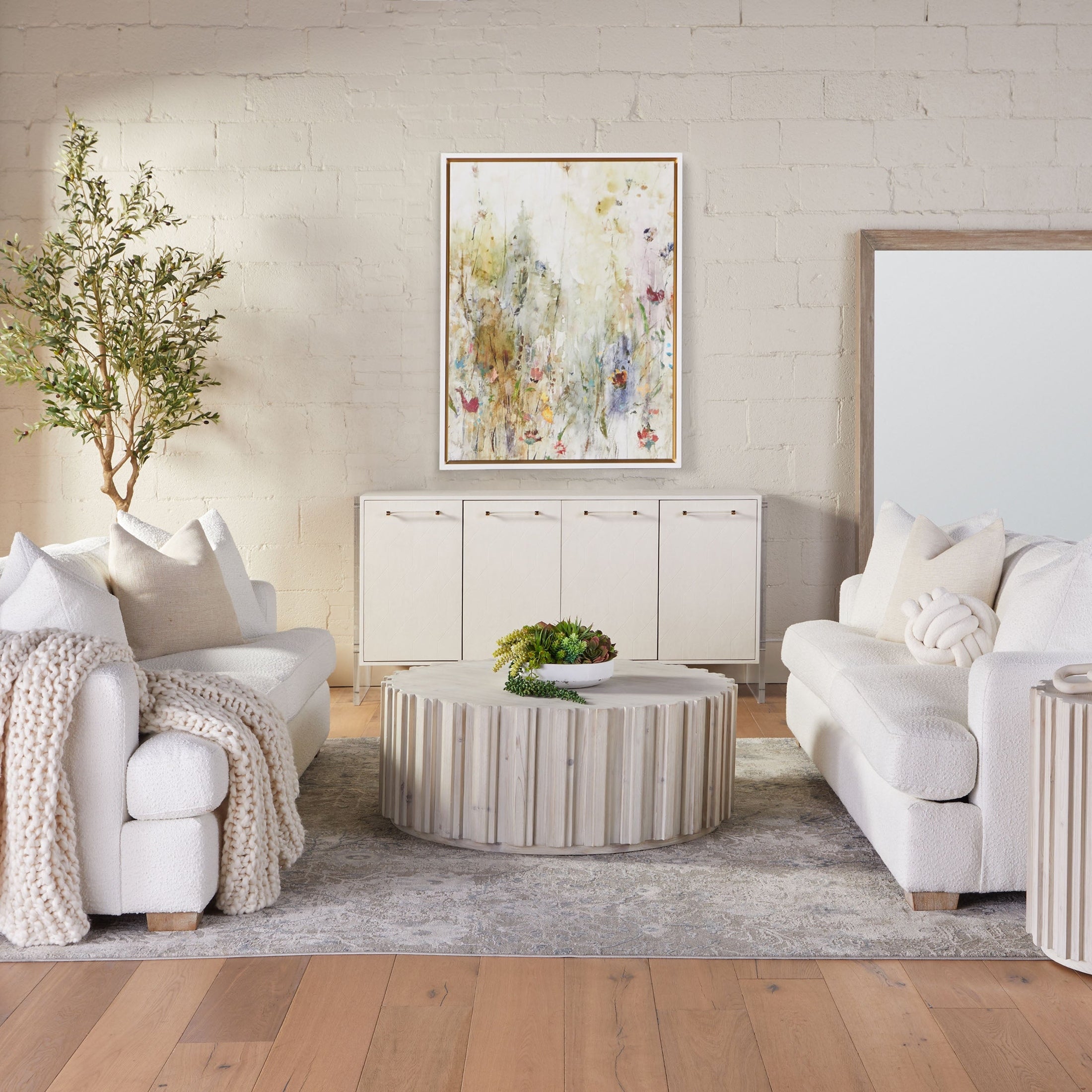 Living room with neutral sofas, textured rug, wooden fluted round coffee table, and abstract wall art.