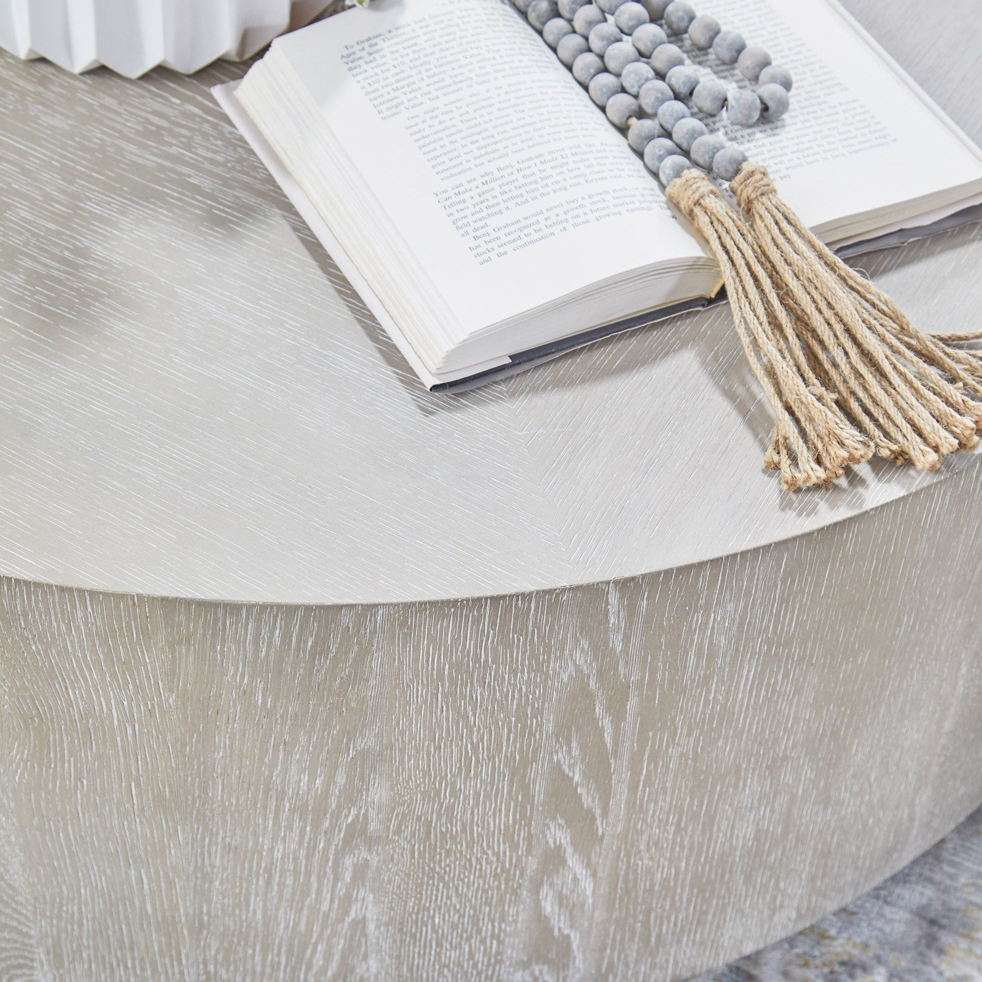 Round Roto Large Coffee Table in natural gray oak veneer with book and beads on top by Essentials for Living