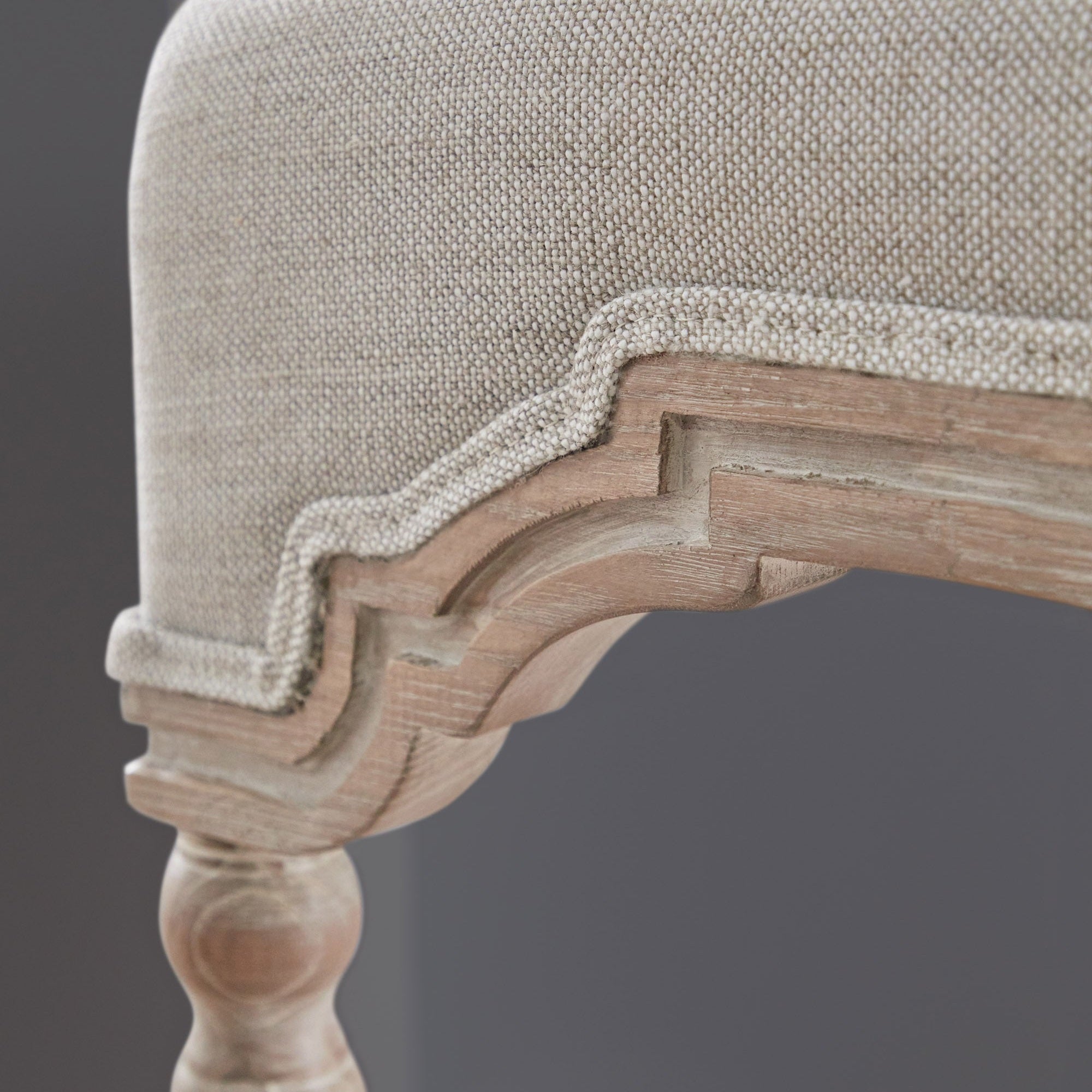 Close-up of Rue Counter Stool showing bisque linen upholstery and carved natural gray ash wood detailing by Essentials for Living