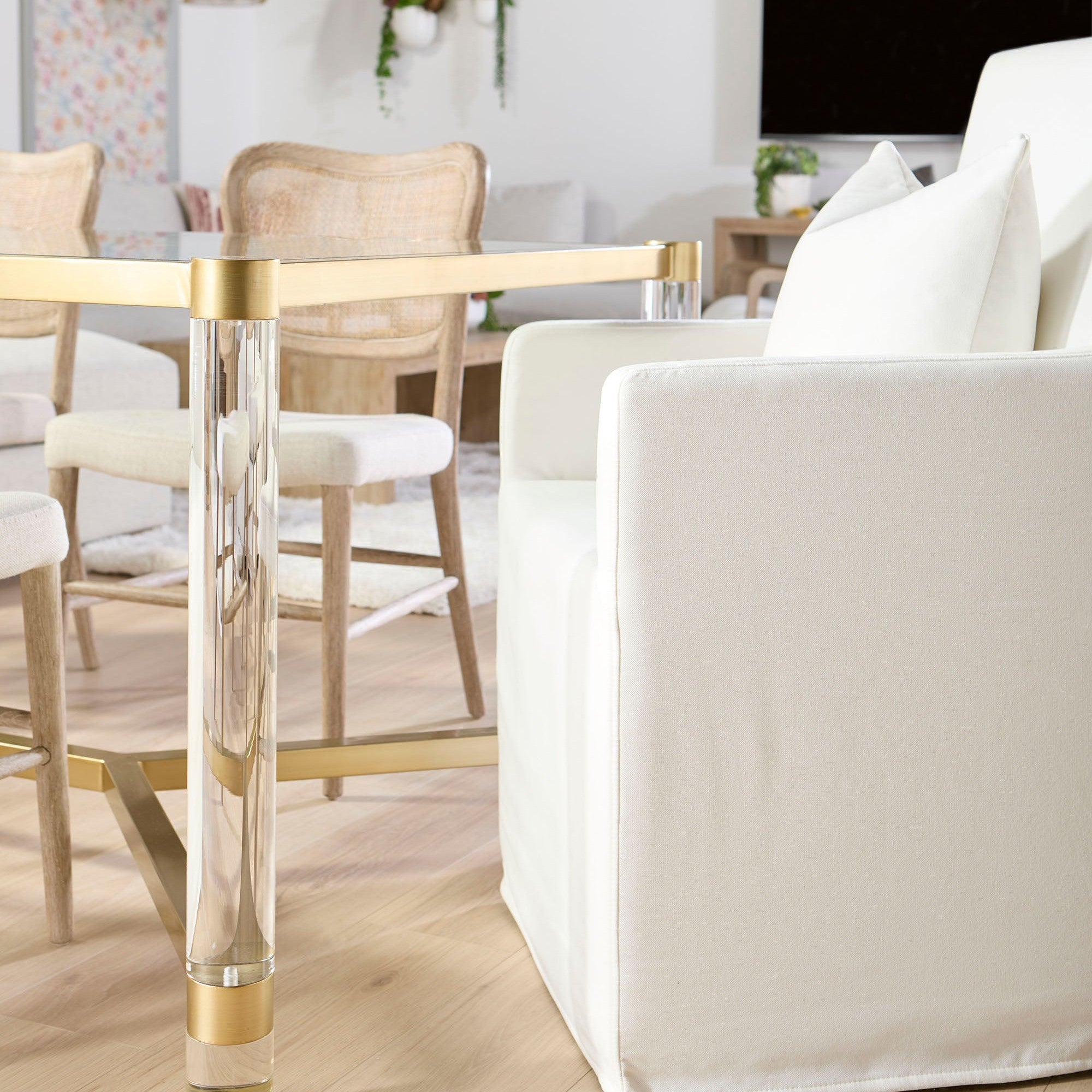 Essentials for Living white Shelter slipcover arm chair with casters beside a glass and gold dining table in bright room